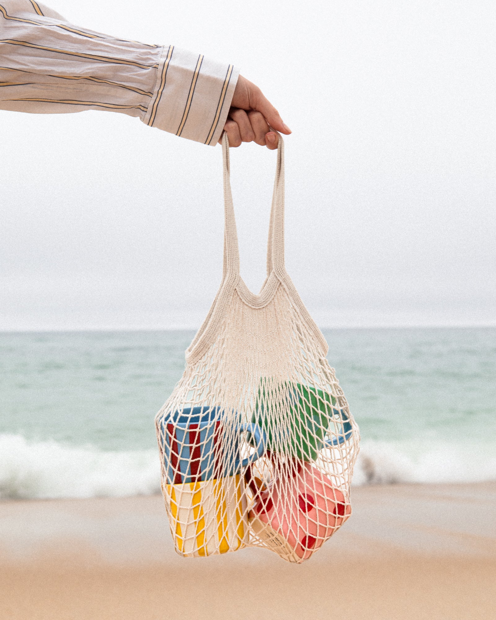 Eine Hand hält ein Netz mit bunten Objekten am Strand.