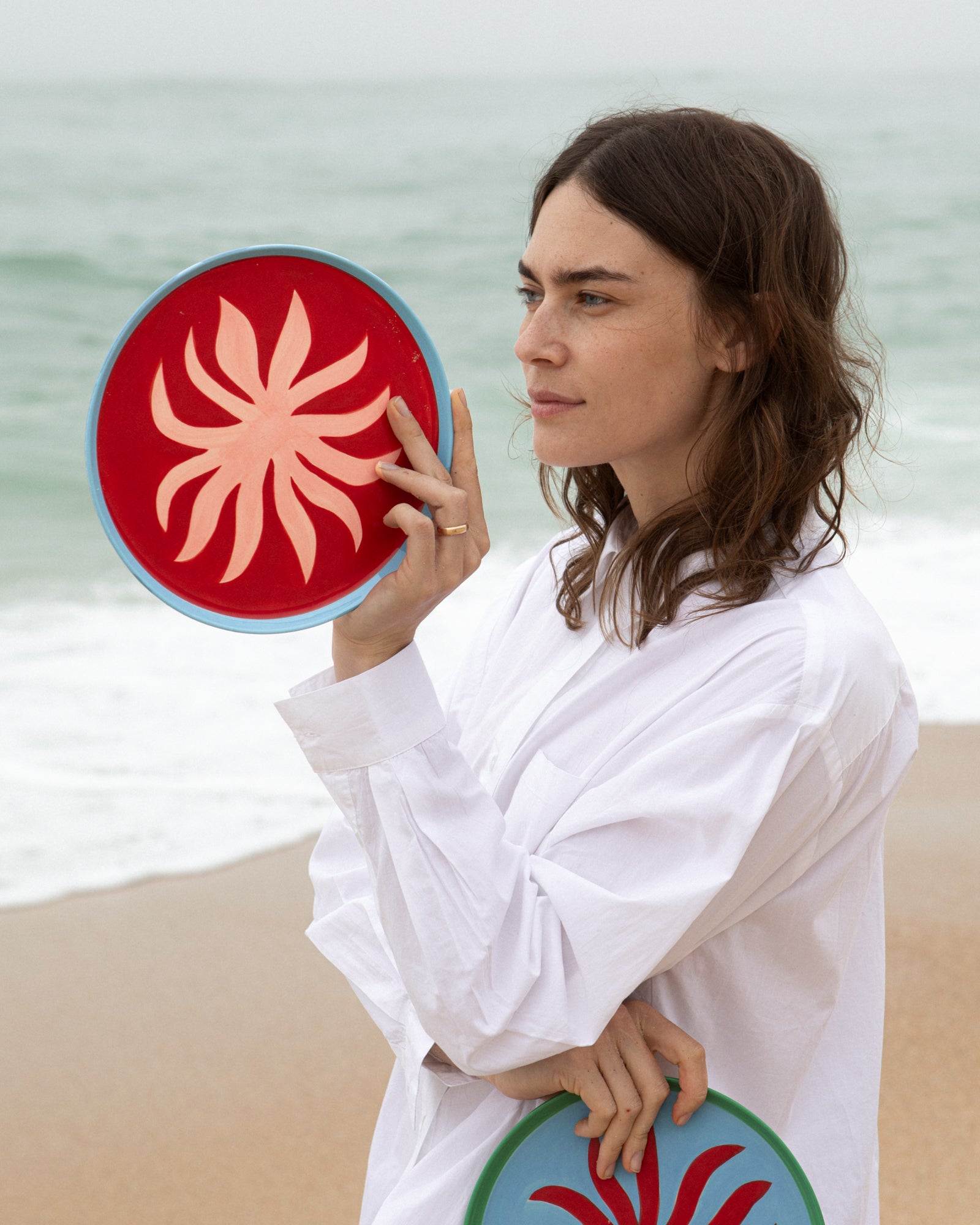 Frau am Strand hält ein buntes Frisbee, das ein stilisiertes Muster zeigt.