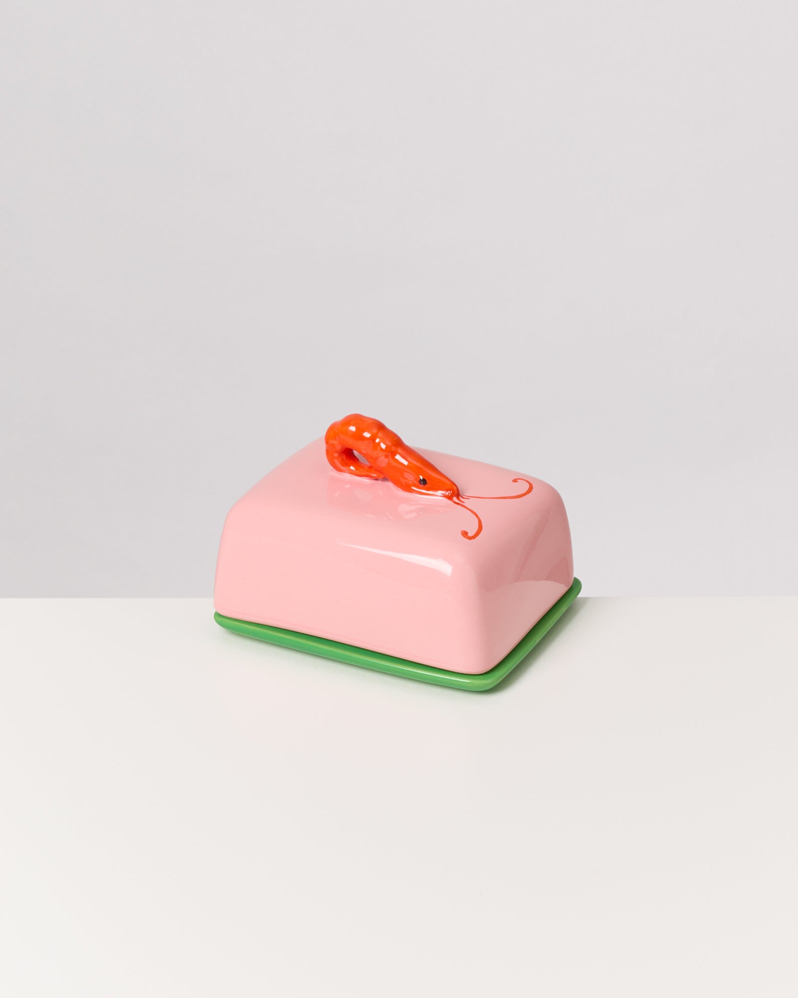 Eine rosa Butterdose mit einem orangefarbenen Garnelen-Dekor auf einem grünen Untersetzer.