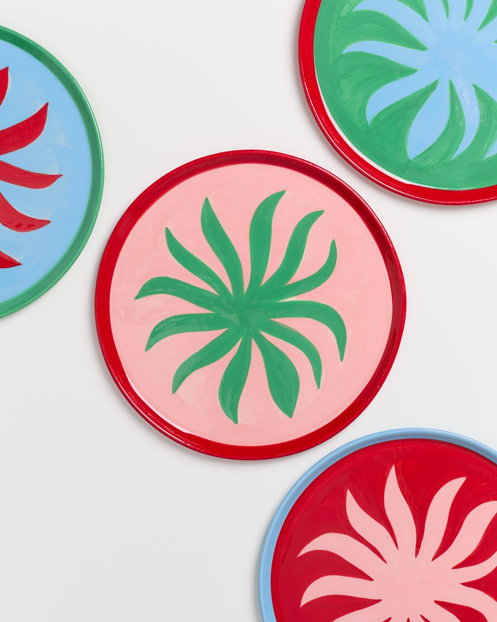 Bunte Teller mit abstrakten Pflanzenmotiven in Rot, Grün, Rosa und Blau auf weißem Hintergrund.