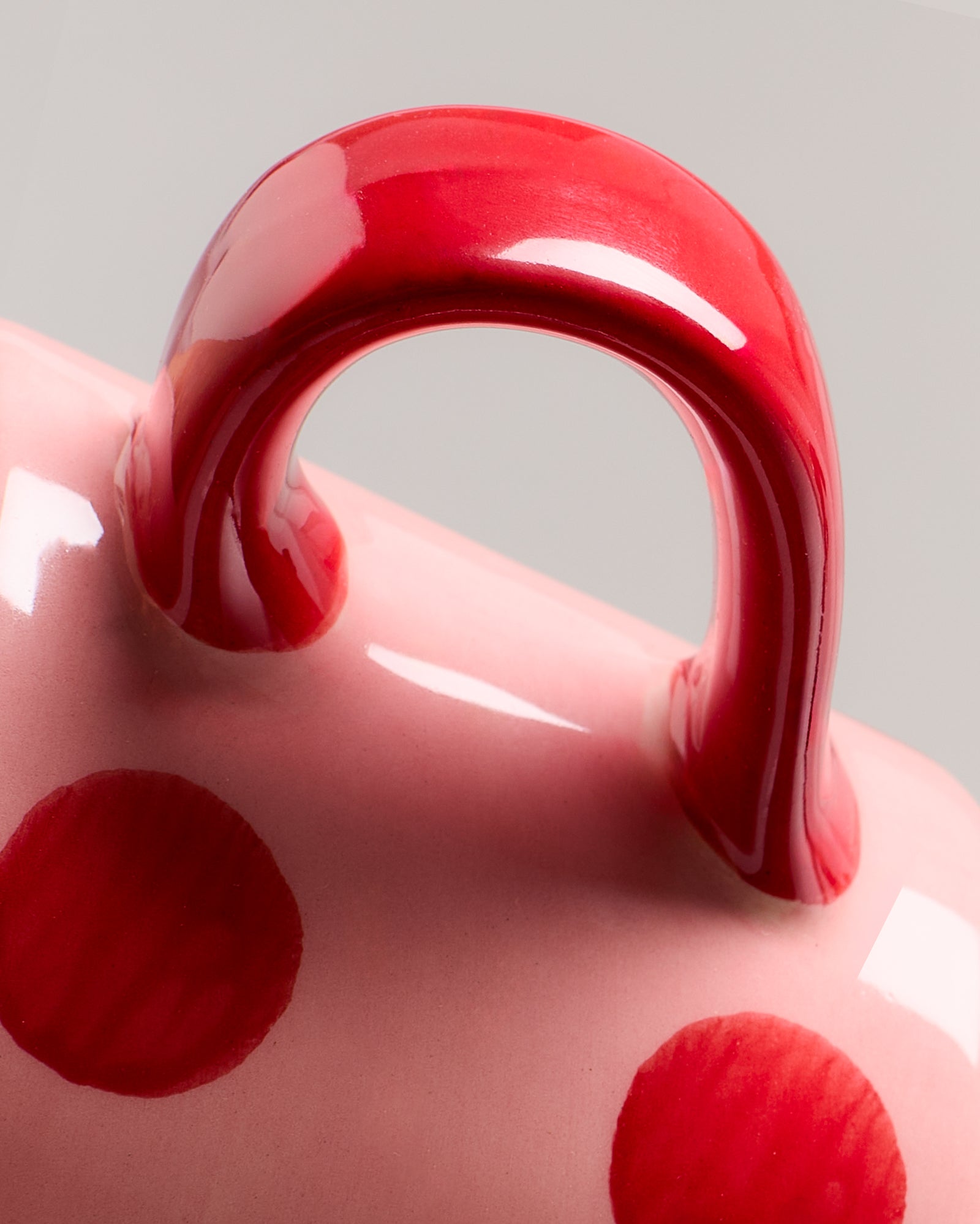 Nahaufnahme eines rosafarbenen Keramikgegenstands mit roten Punkten und einem roten Henkel.