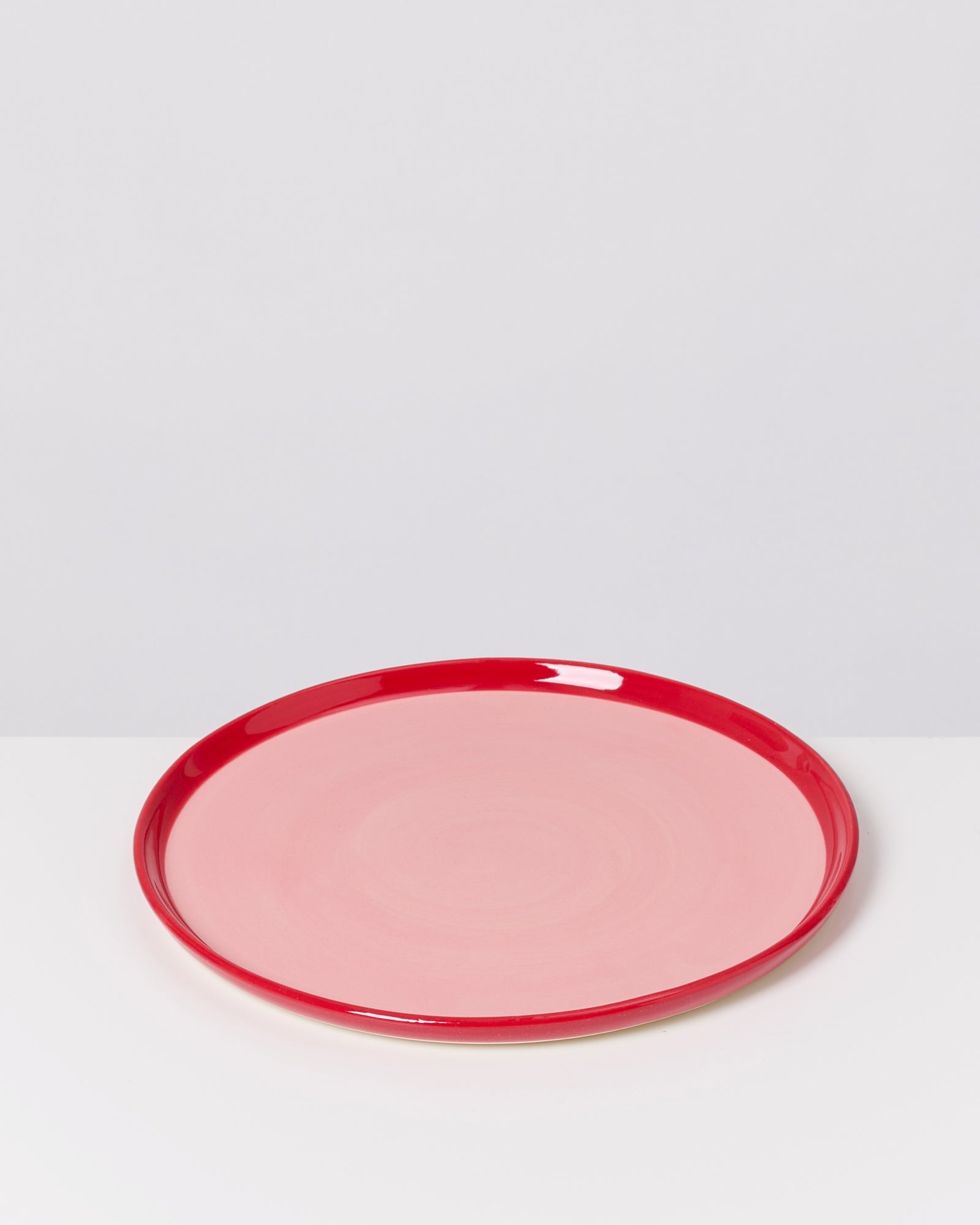 Runder Teller mit rotem Rand und rosa Mitte auf weißem Hintergrund.