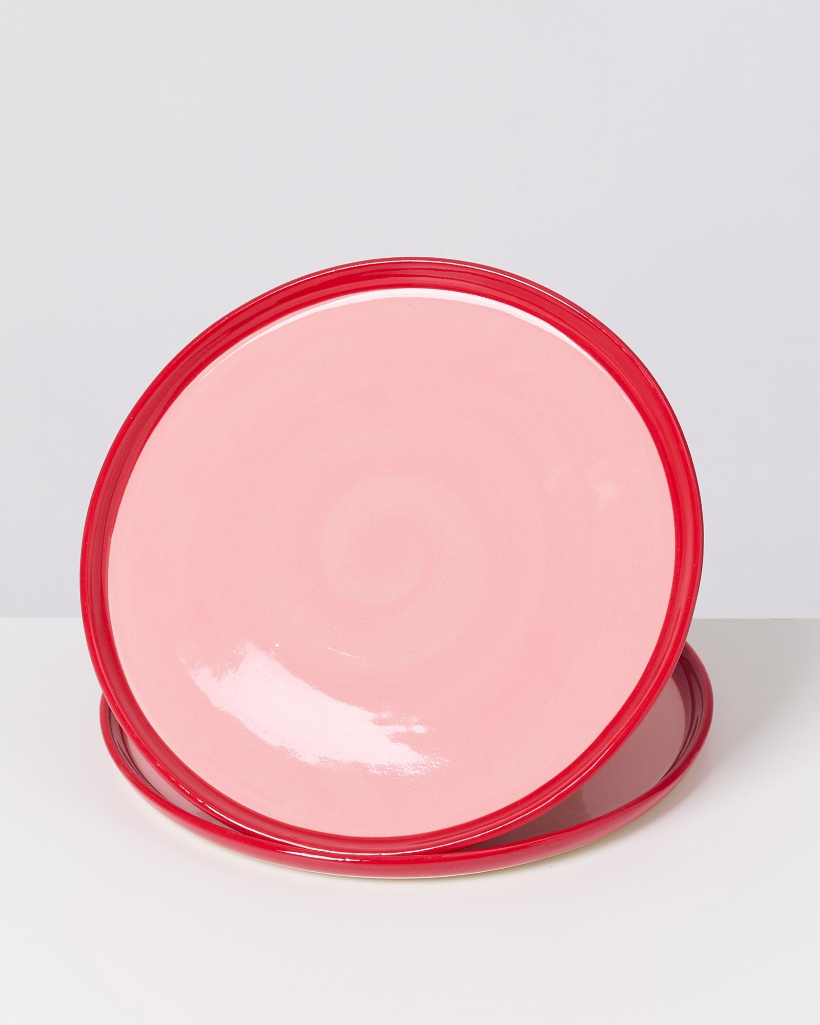 Zwei runde, rosafarbene Teller mit rotem Rand auf weißem Hintergrund.