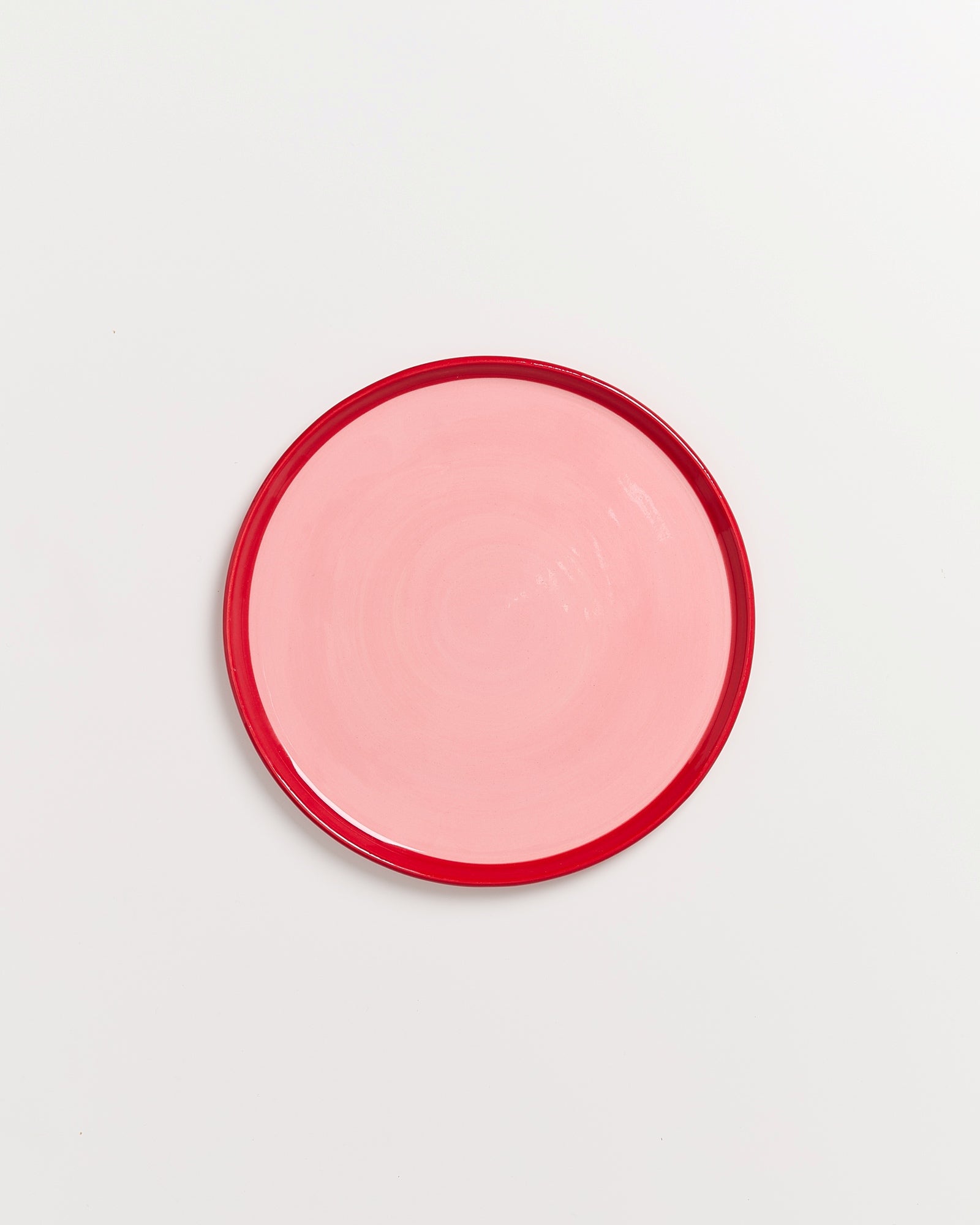 Ein pinkfarbener Teller mit rotem Rand auf weißem Hintergrund.