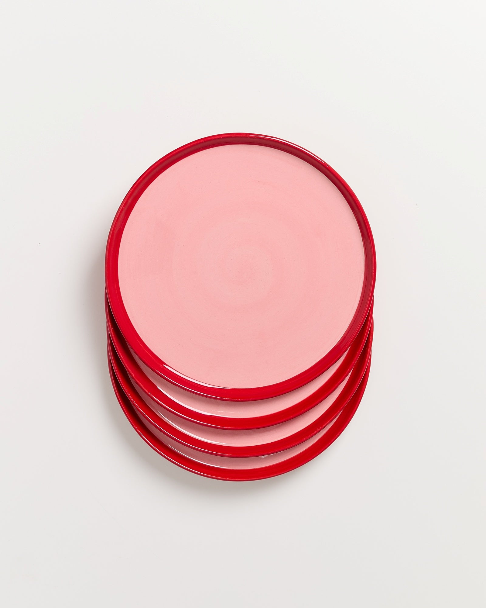 Ein Stapel rosafarbener Teller mit rotem Rand auf weißem Hintergrund.