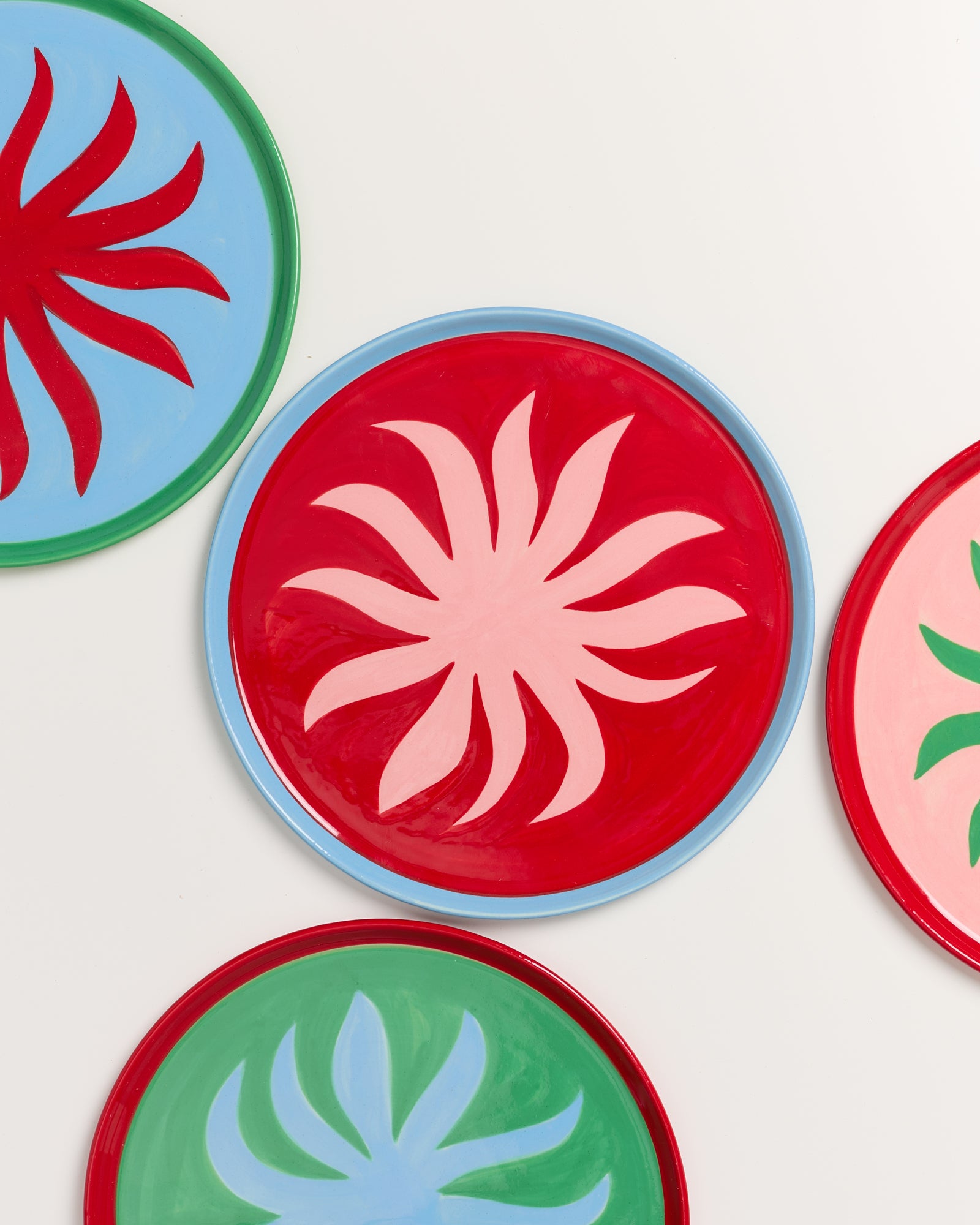Bunte Teller mit abstrakten floralen Mustern in Rot, Grün und Blau auf weißem Hintergrund.
