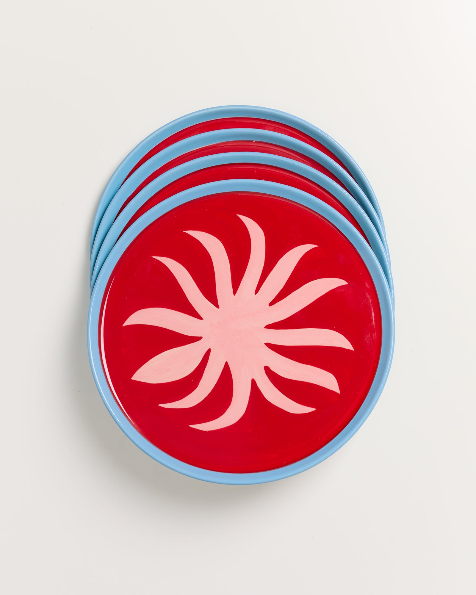 Vier rote Teller mit blauen Rändern und weißem Blumenmuster, gestapelt auf einer weißen Oberfläche.