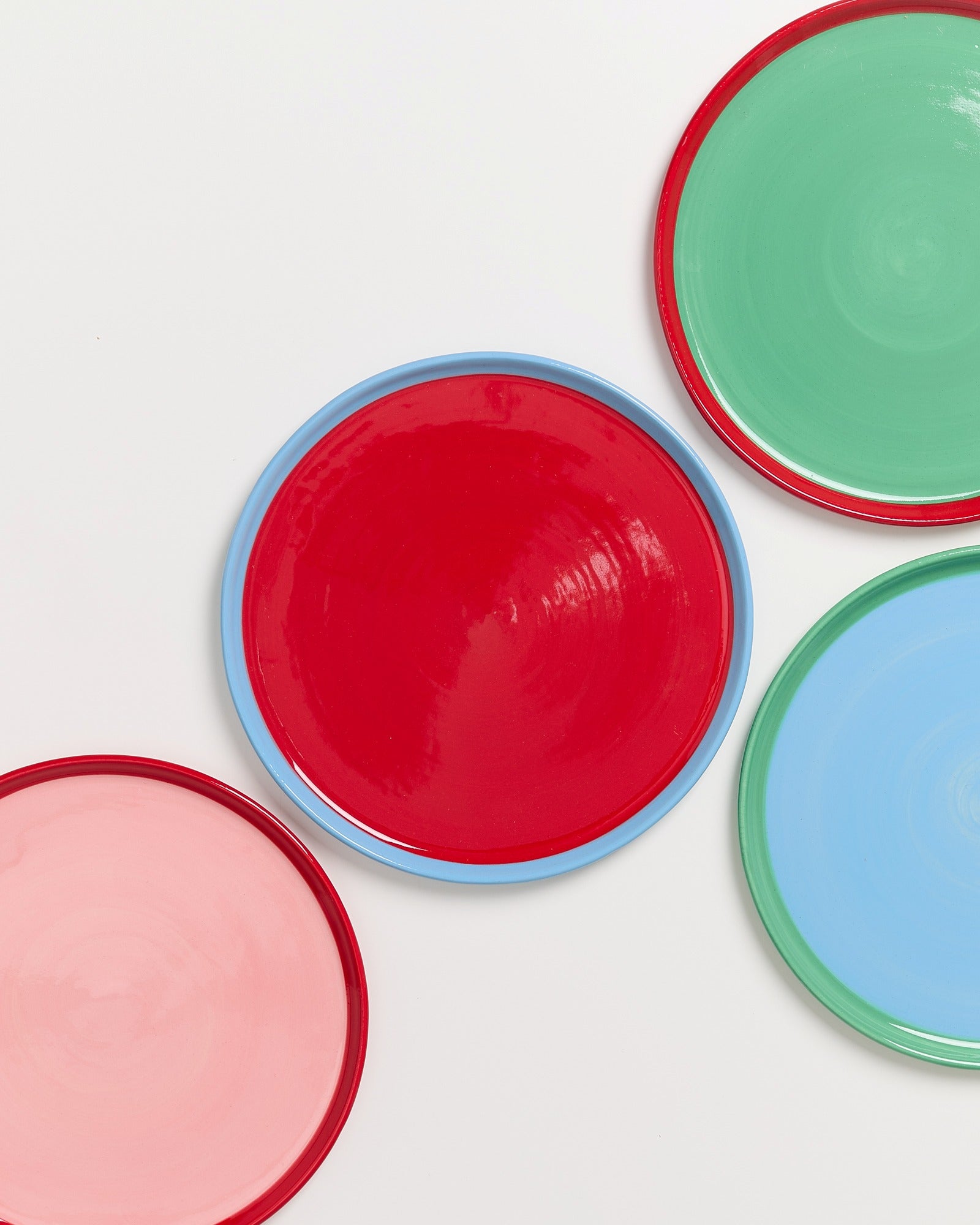 Vier bunte Teller in Rot, Grün, Blau und Rosa liegen auf einem weißen Hintergrund.
