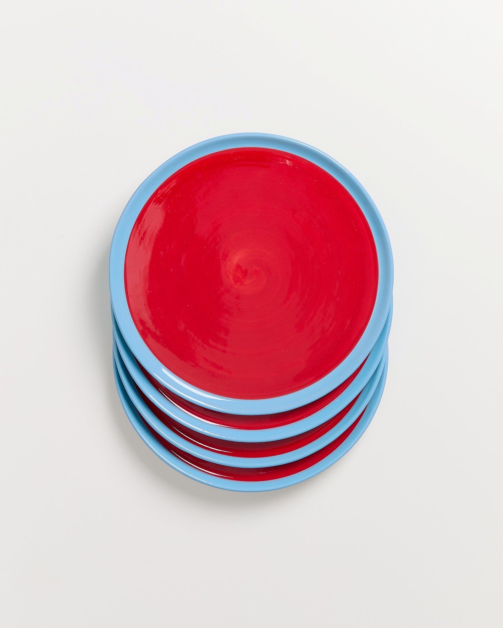 Ein Stapel roter Teller mit blauem Rand auf einem weißen Hintergrund.