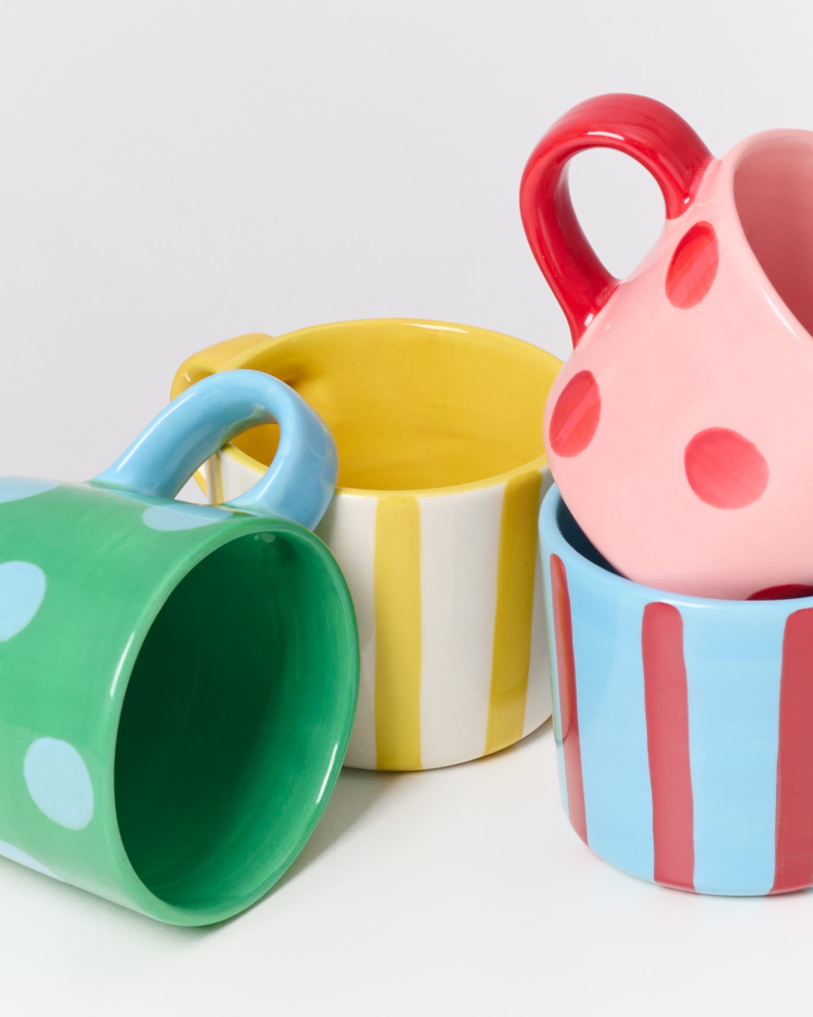 Bunte Tassen mit verschiedenen Mustern, wie Punkte und Streifen, stehen ineinander gestapelt auf einem weißen Hintergrund.