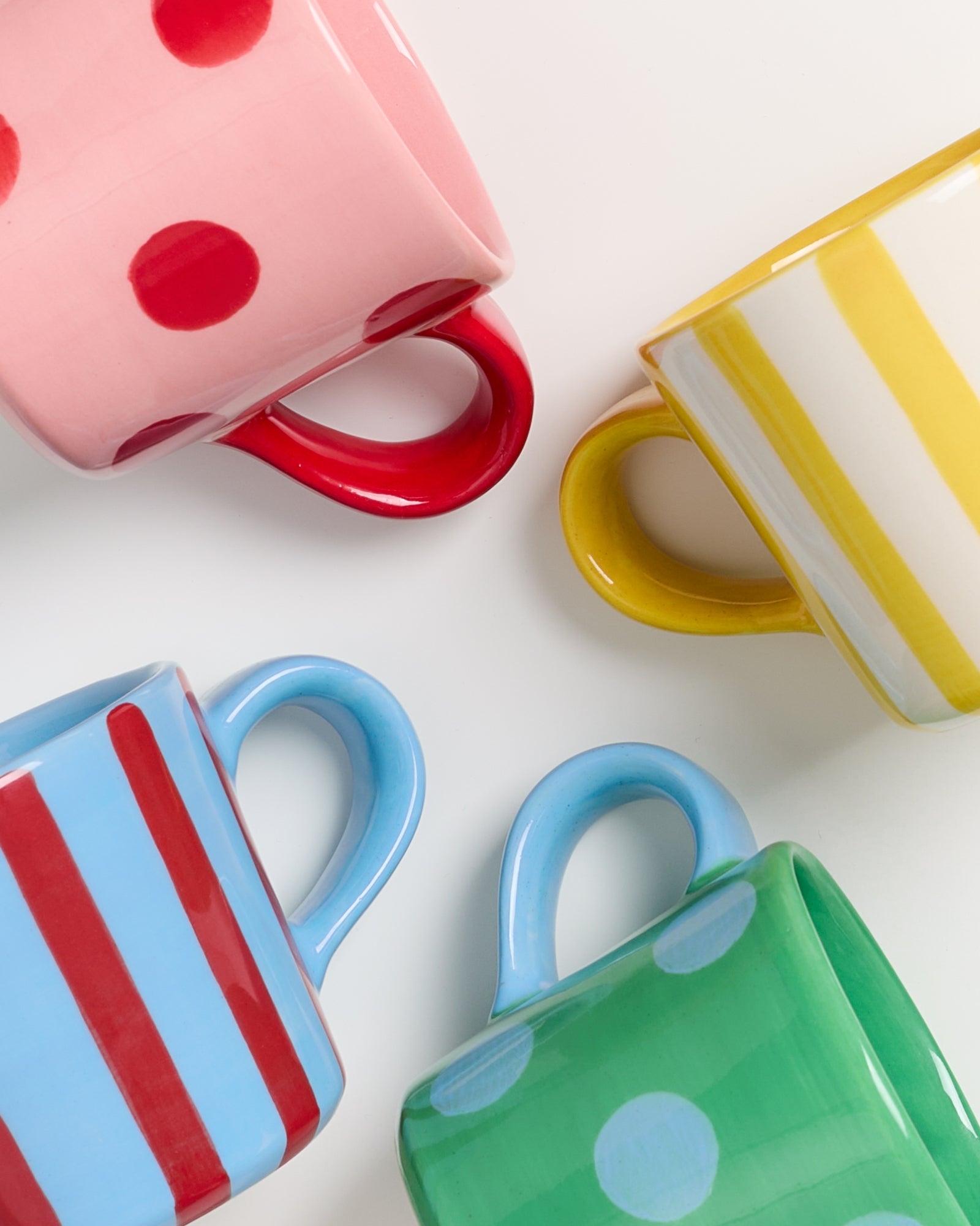 Vier bunt gemusterte Tassen mit verschiedenen Designs liegen auf einem weißen Hintergrund.