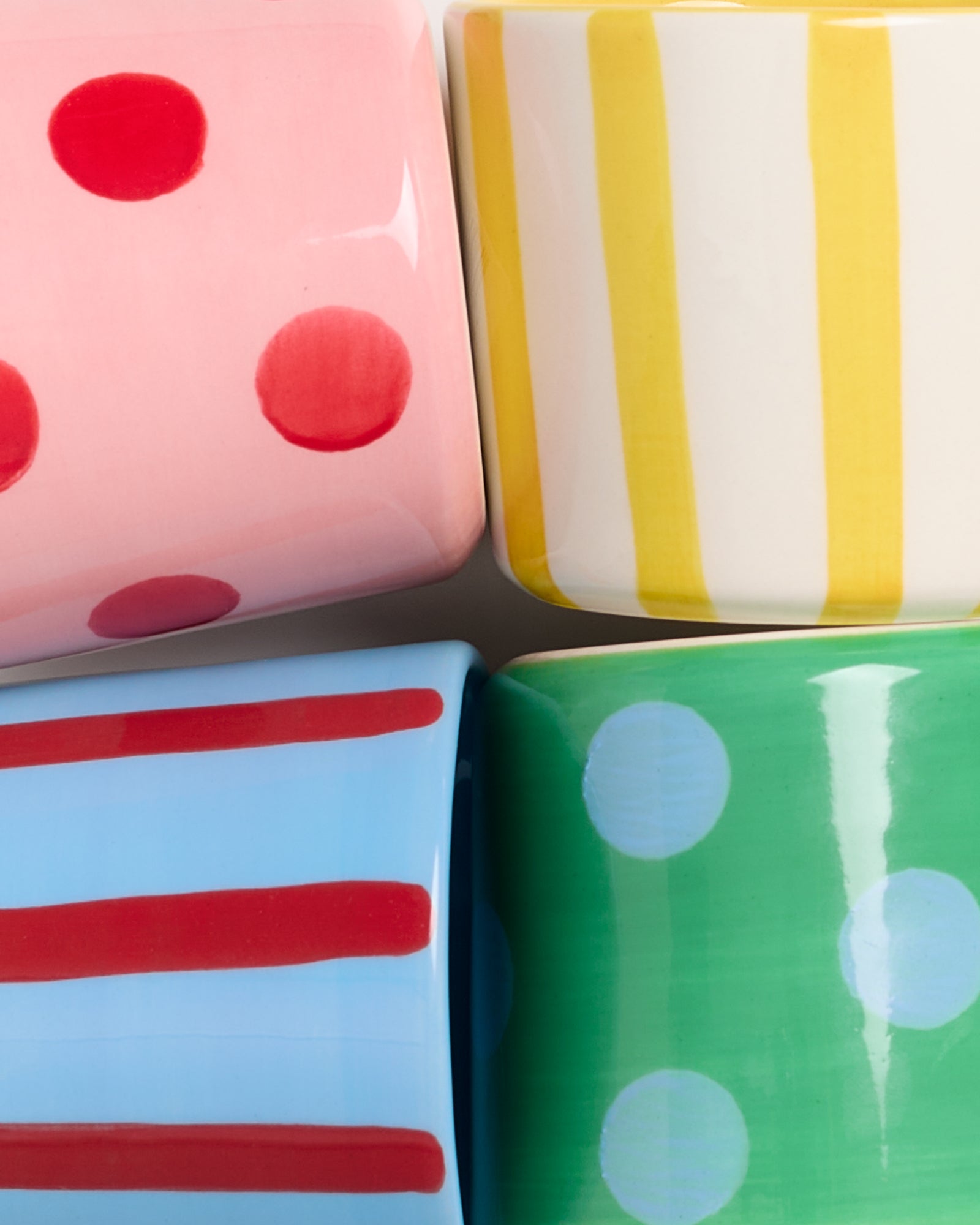 Vier bunte, gemusterte Keramikbecher mit Punkten und Streifen in Rot, Gelb, Blau und Grün.