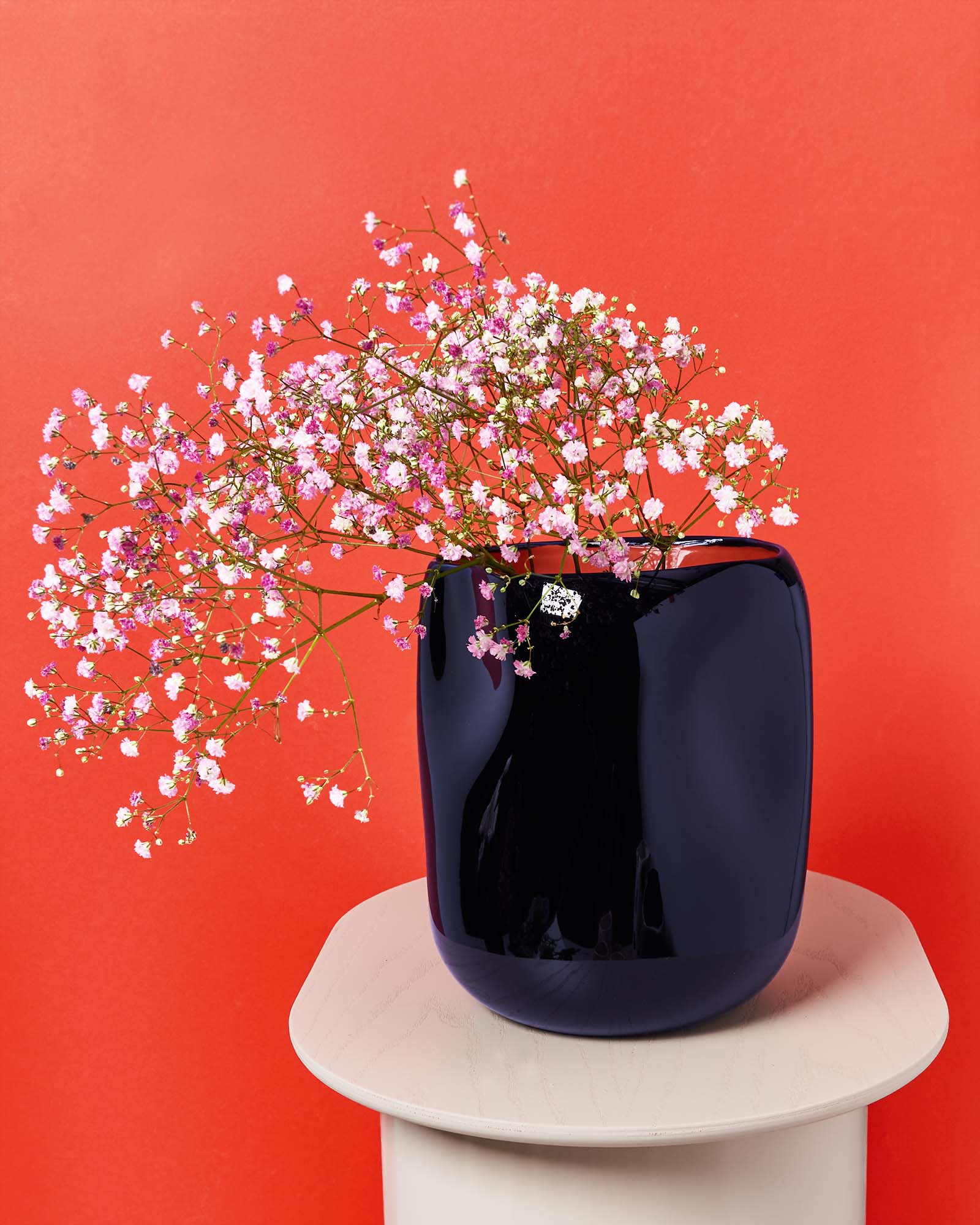 Schwarze Vase mit rosa und weißen Blüten vor einem roten Hintergrund auf einem runden Tisch.