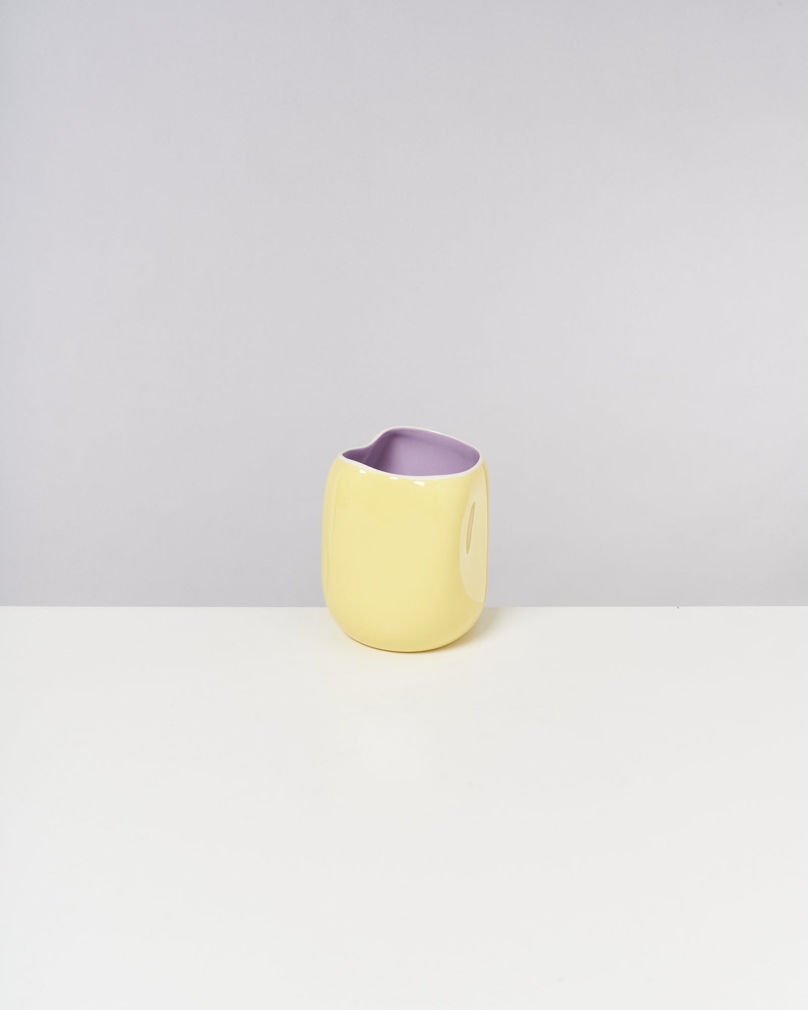 Gelbe Vase mit lila Innenraum auf einem weißen Tisch vor grauem Hintergrund.