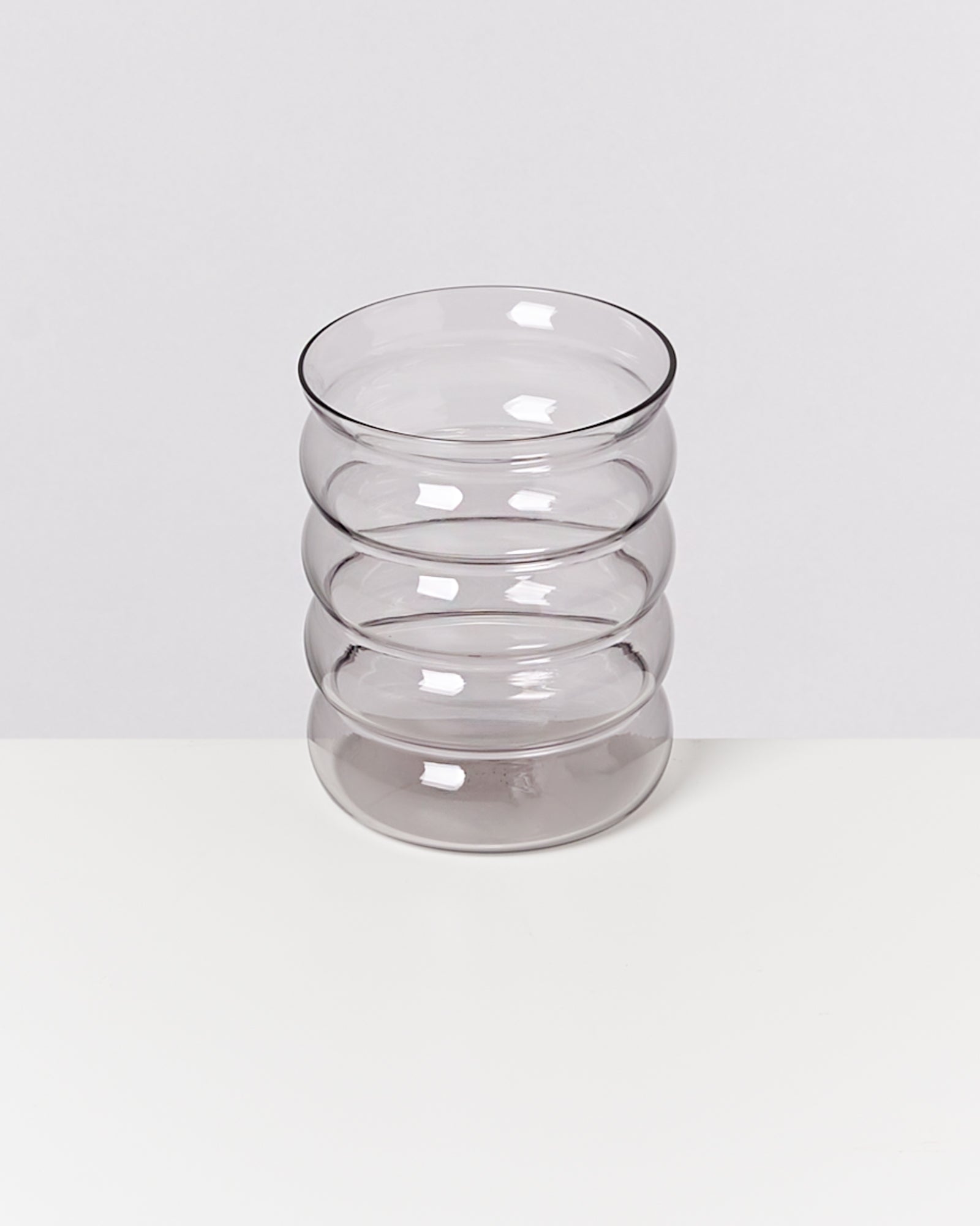 Klares Glas mit geschwungenen Faltlinien, auf einem weißen Hintergrund stehend.