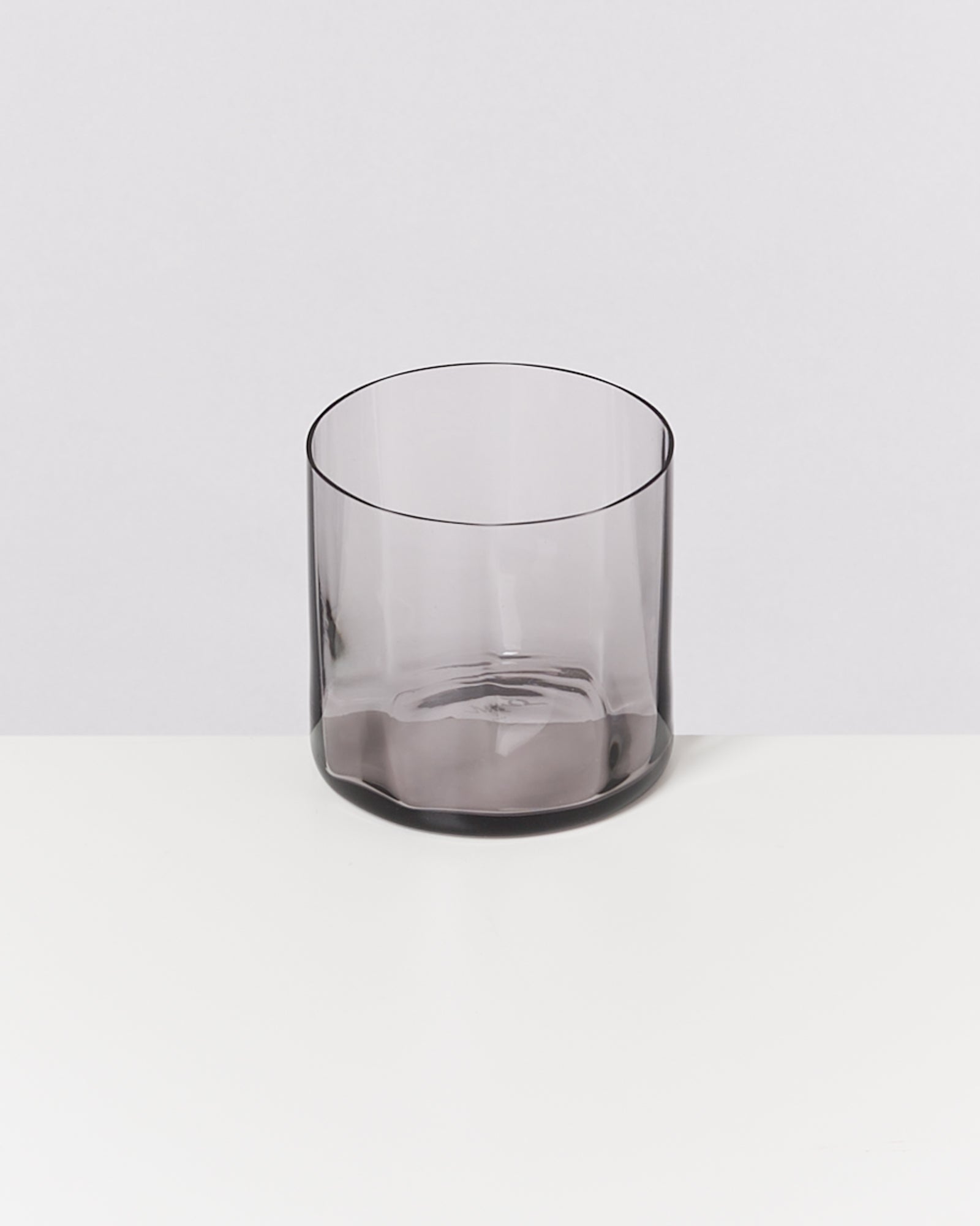 Graues, durchsichtiges Trinkglas auf weißem Hintergrund.