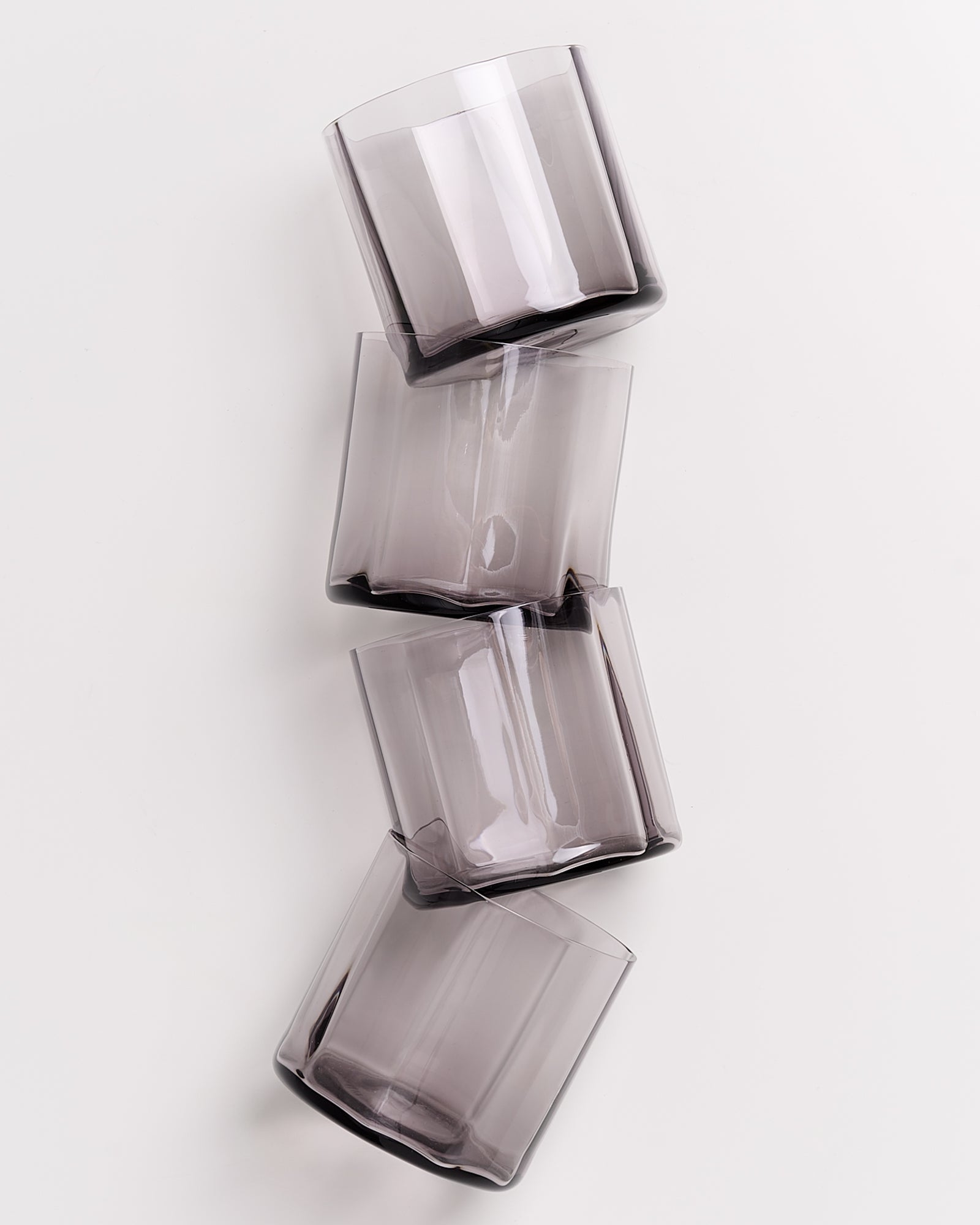 Vier gestapelte, leicht schräg übereinander liegende, durchsichtige graue Gläser auf weißem Hintergrund.