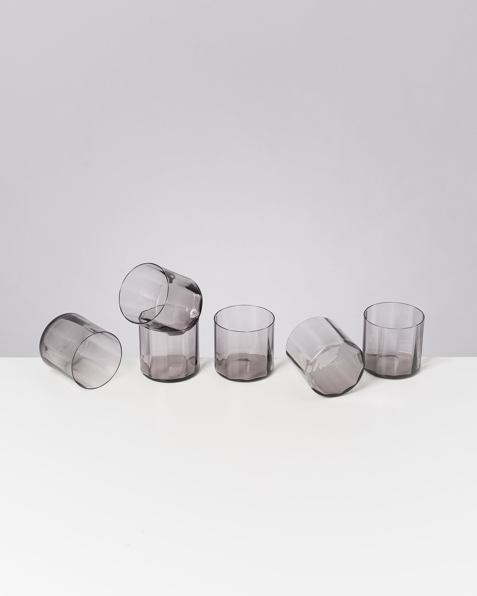 Fünf durchsichtige Gläser auf einem weißen Tisch; drei stehen, zwei liegen.