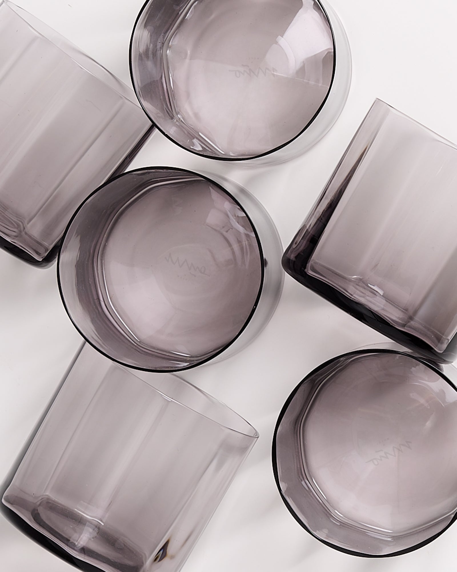 Sechs durchsichtige, graue Gläser liegen unregelmäßig verteilt auf einer weißen Fläche.