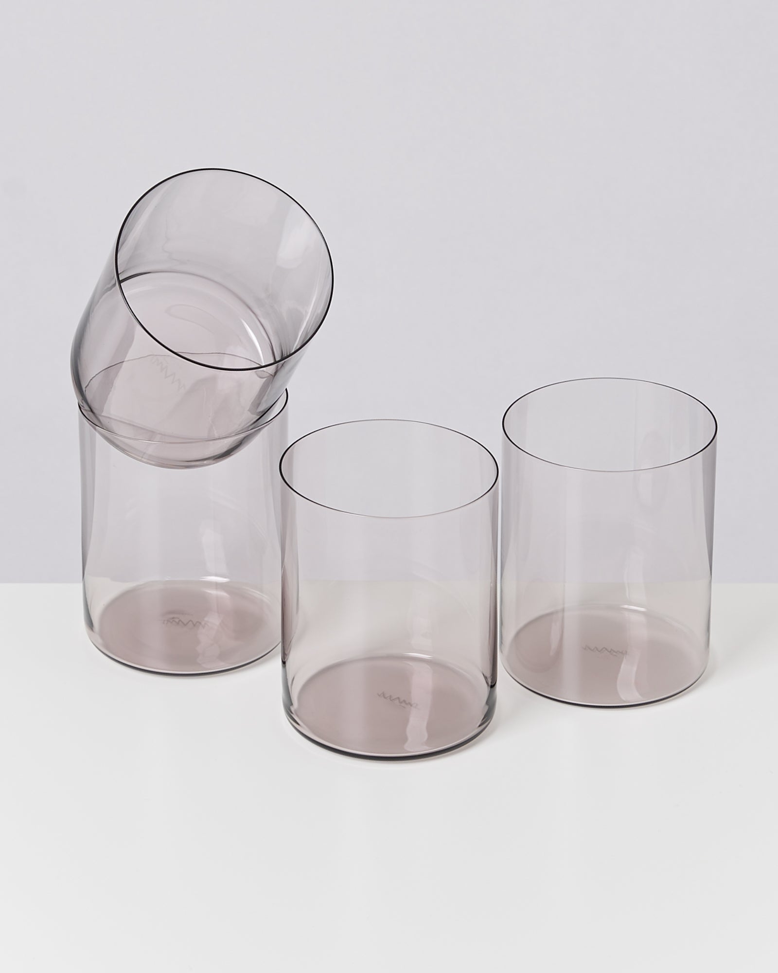 Vier durchsichtige Gläser, von denen eines über die anderen balanciert, stehen auf einer weißen Oberfläche.