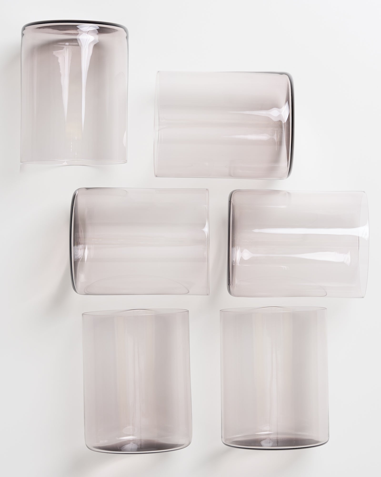 Sechs klare, zylinderförmige Gläser in zwei Reihen auf einer weißen Oberfläche arrangiert.