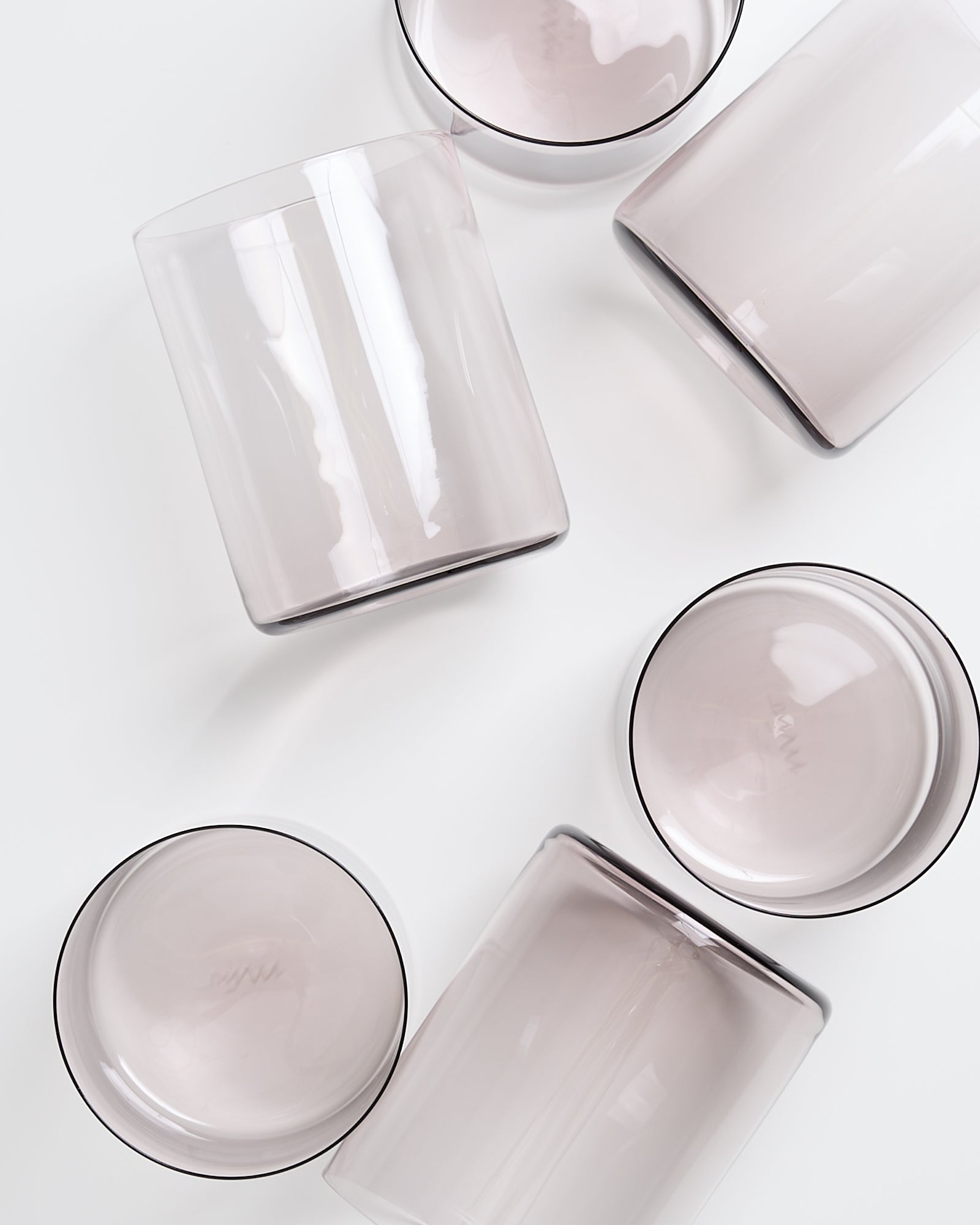 Fünf transparente, zylindrische Gläser liegen auf einer weißen Oberfläche verstreut.