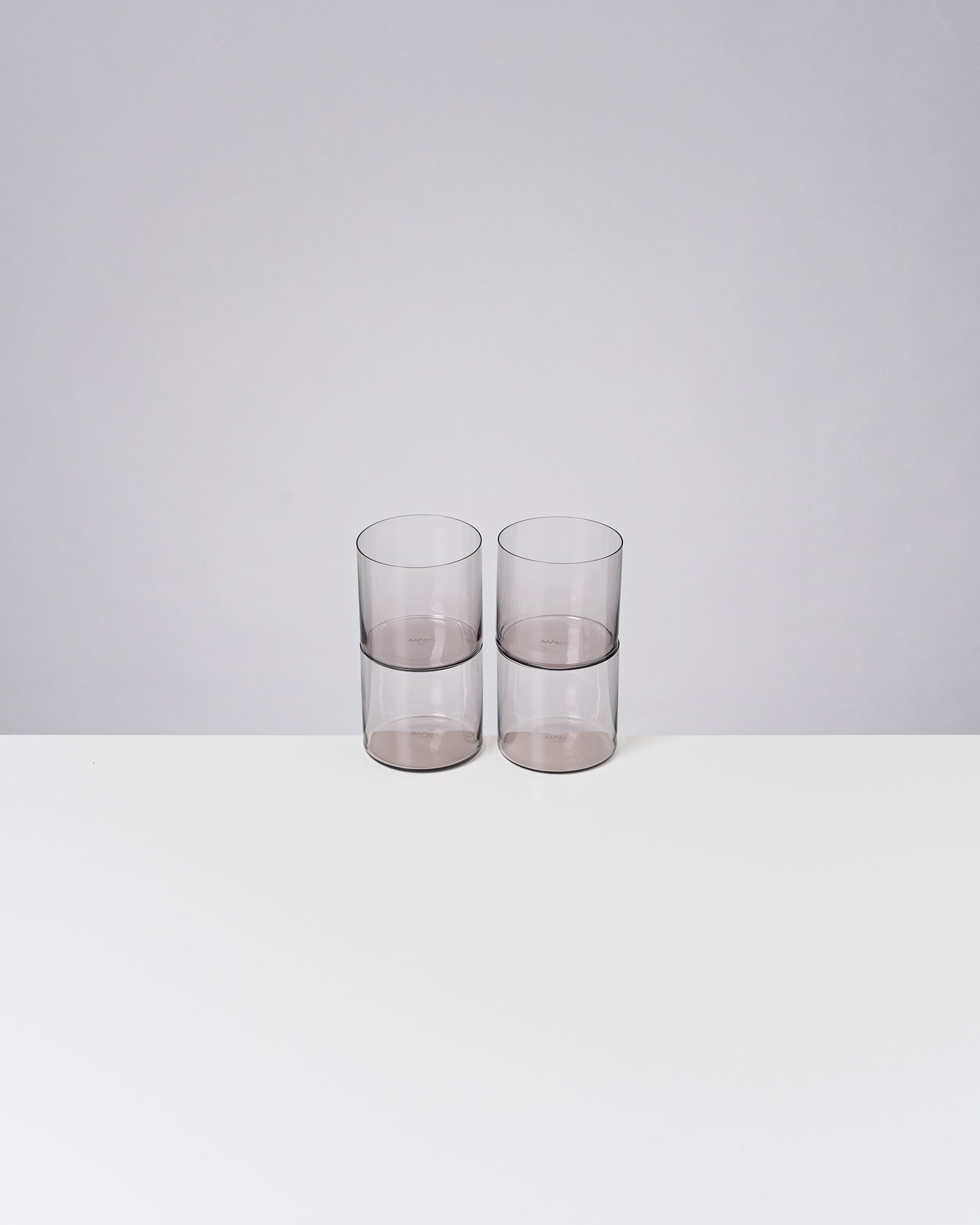 Zwei transparente, übereinander gestapelte Gläser auf einem weißen Tisch vor grauem Hintergrund.
