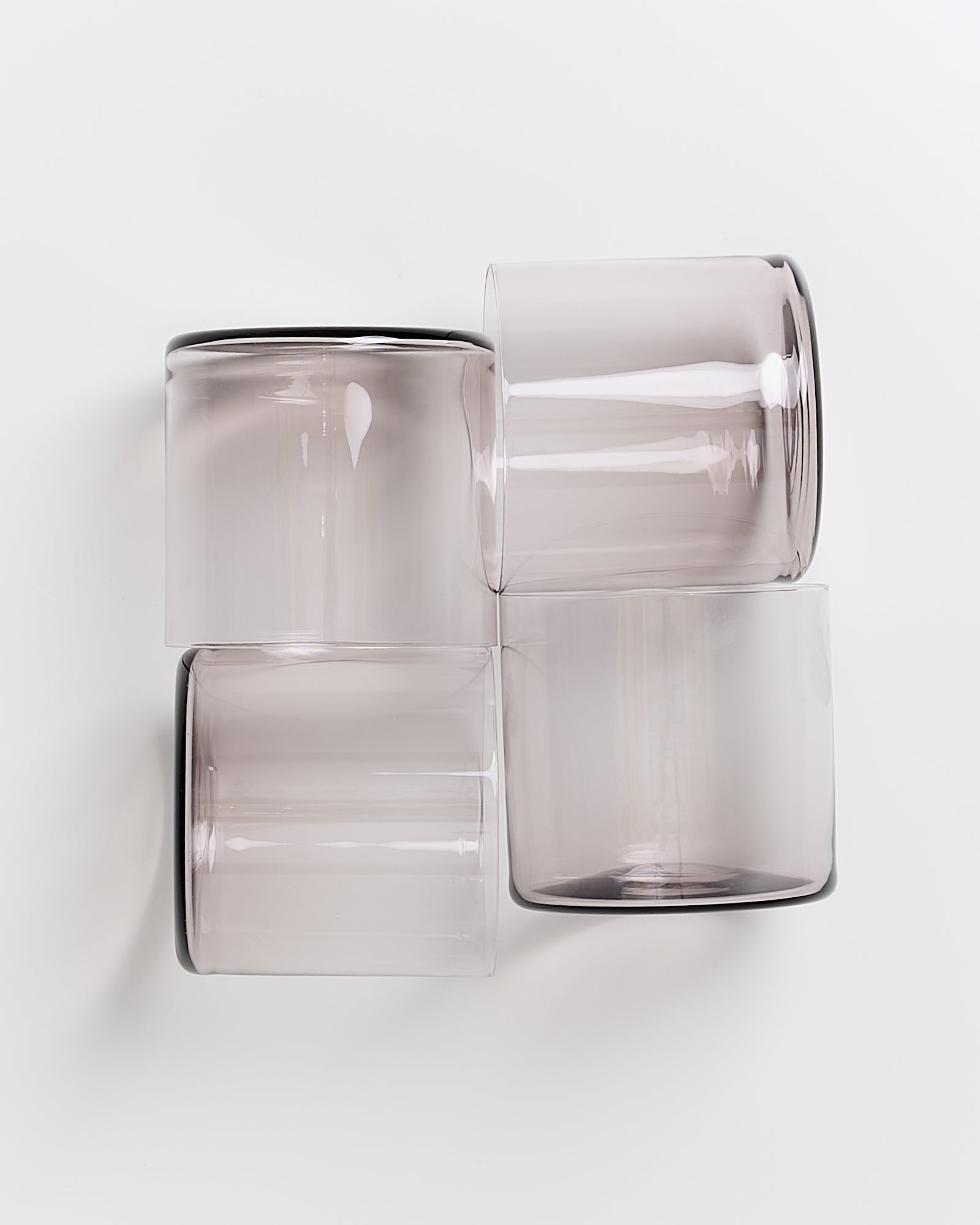 Vier graue, zylindrische Glasbecher liegen auf der Seite und bilden ein Vierer-Cluster auf weißem Hintergrund.