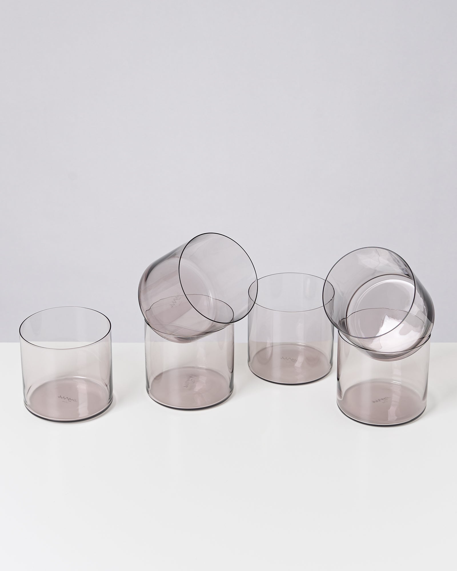 Fünf durchsichtige, graue Gläser auf einem weißen Untergrund, zwei davon liegen schräg auf den anderen.
