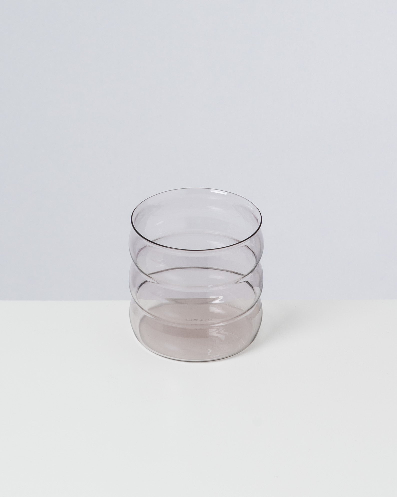 Graues, gestapeltes Glas mit wellenartigem Design auf weißem Hintergrund.