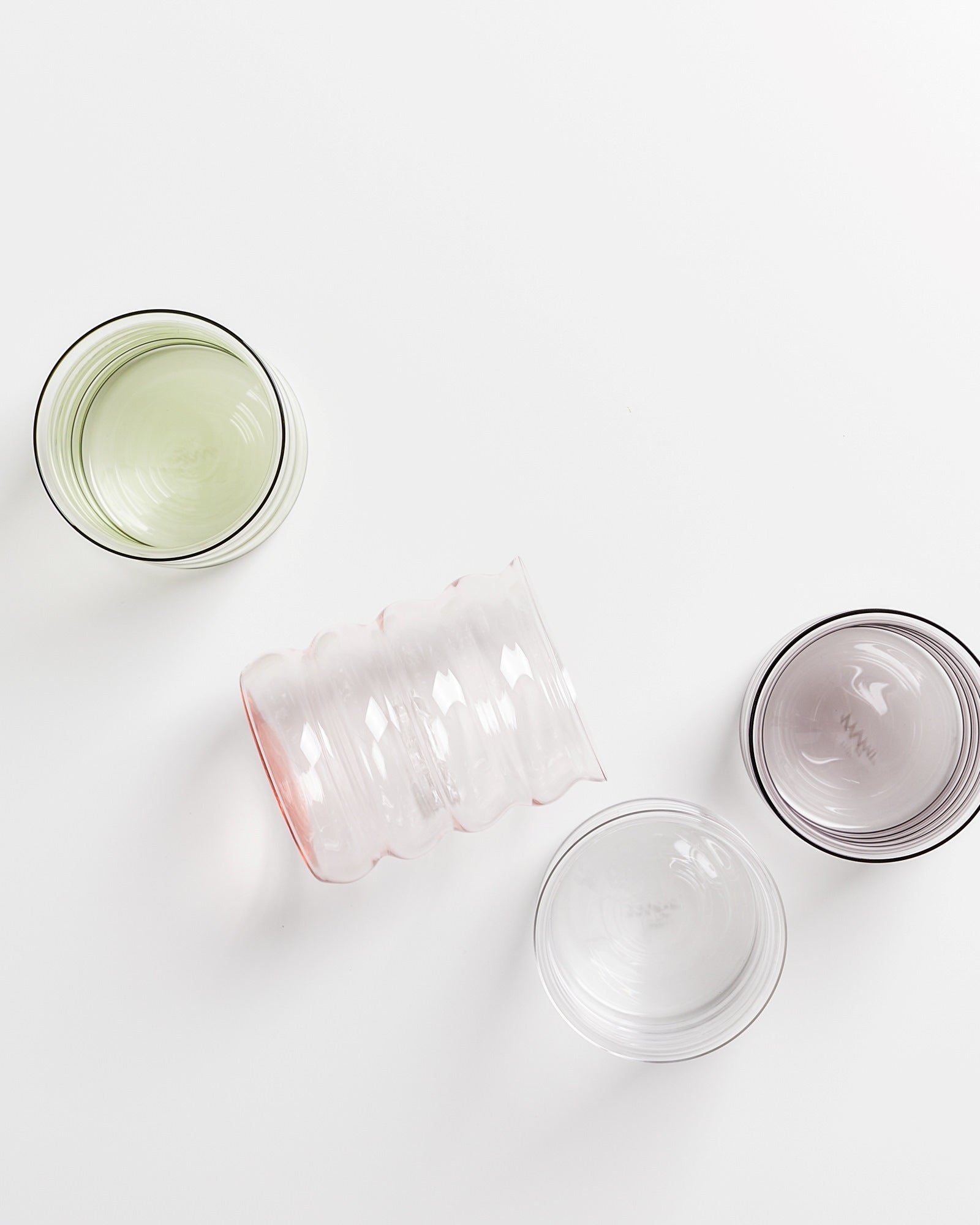 Vier durchsichtige, farbige Gläser in verschiedenen Formen auf einem weißen Hintergrund.