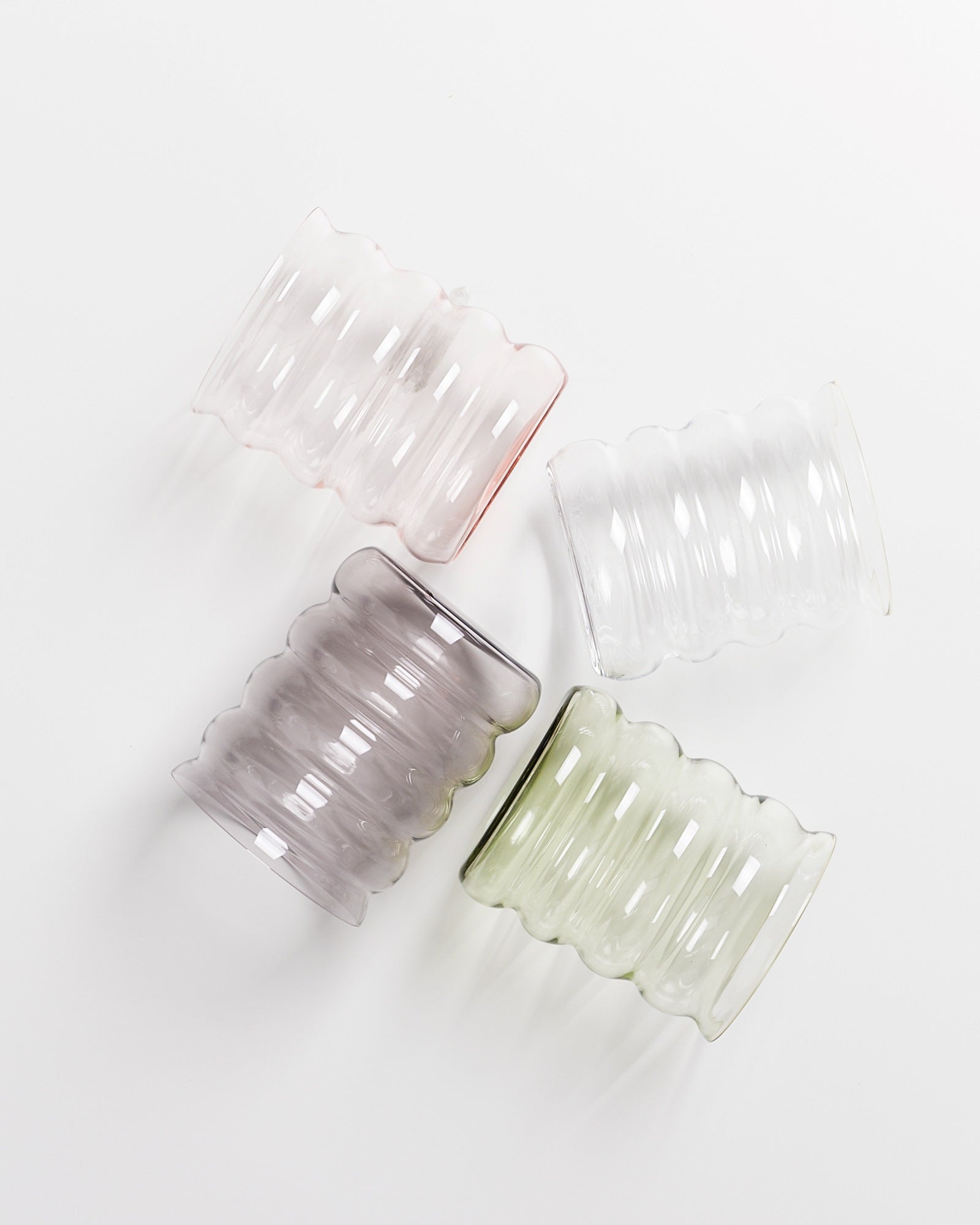 Vier geriffelte Gläser in Pastelltönen, nebeneinander auf weißem Hintergrund liegend.