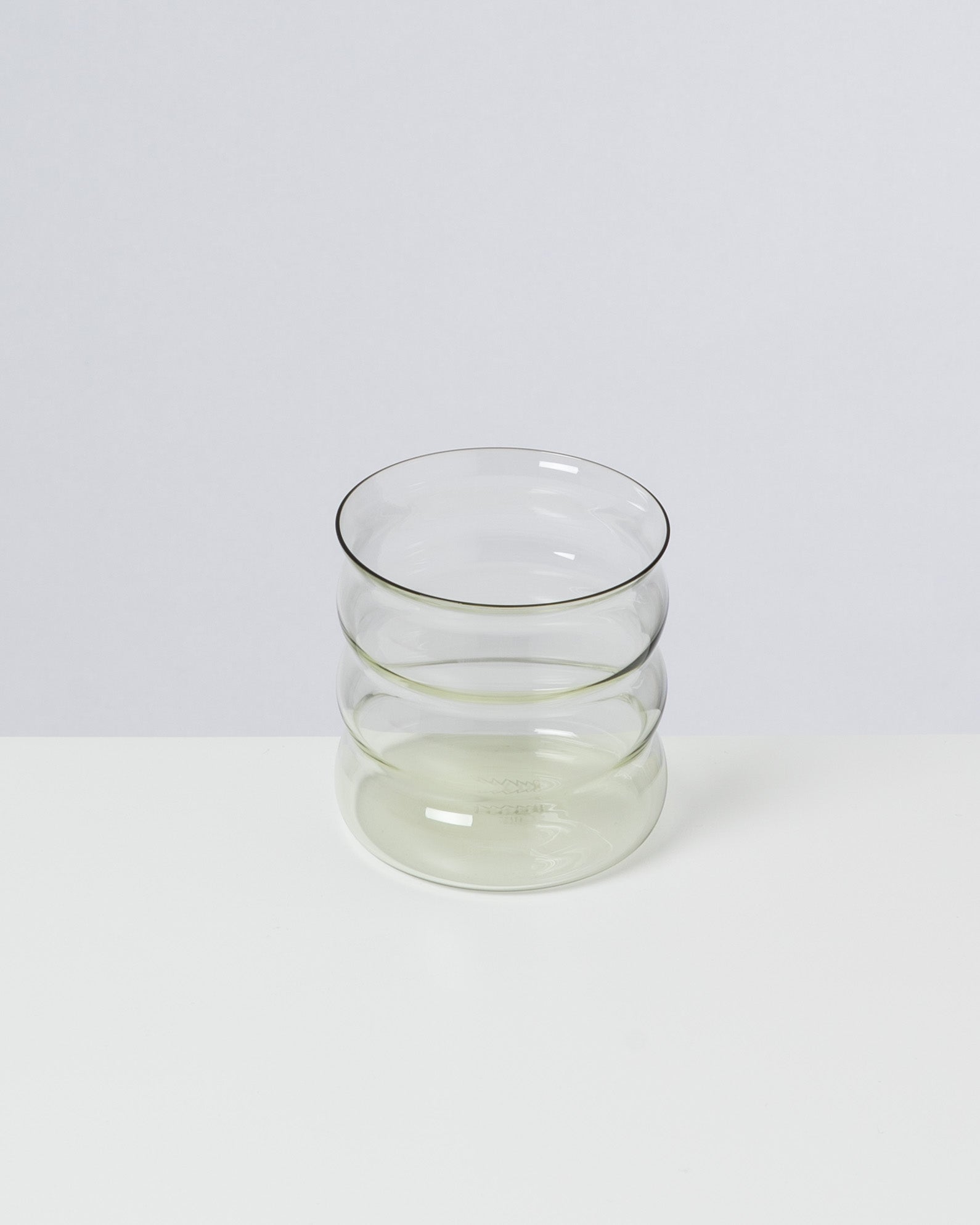 Transparenter Glasbecher mit gerippter Oberfläche auf einem weißen Hintergrund.