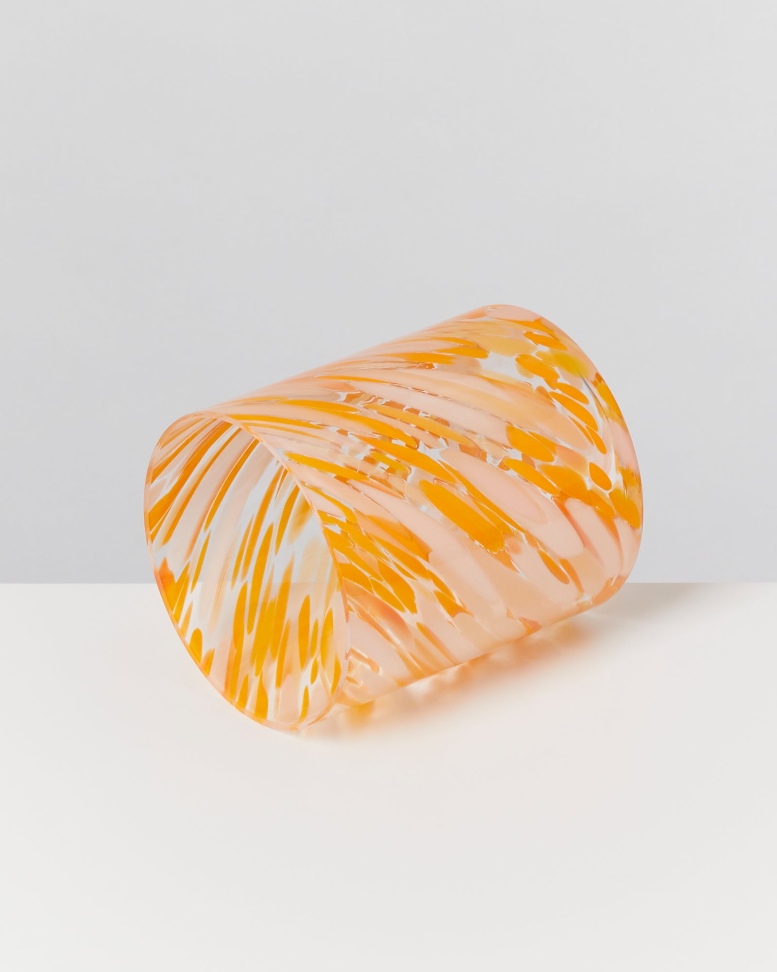 Oranger, gemusterter Glasbecher liegt auf der Seite auf einem weißen Hintergrund.