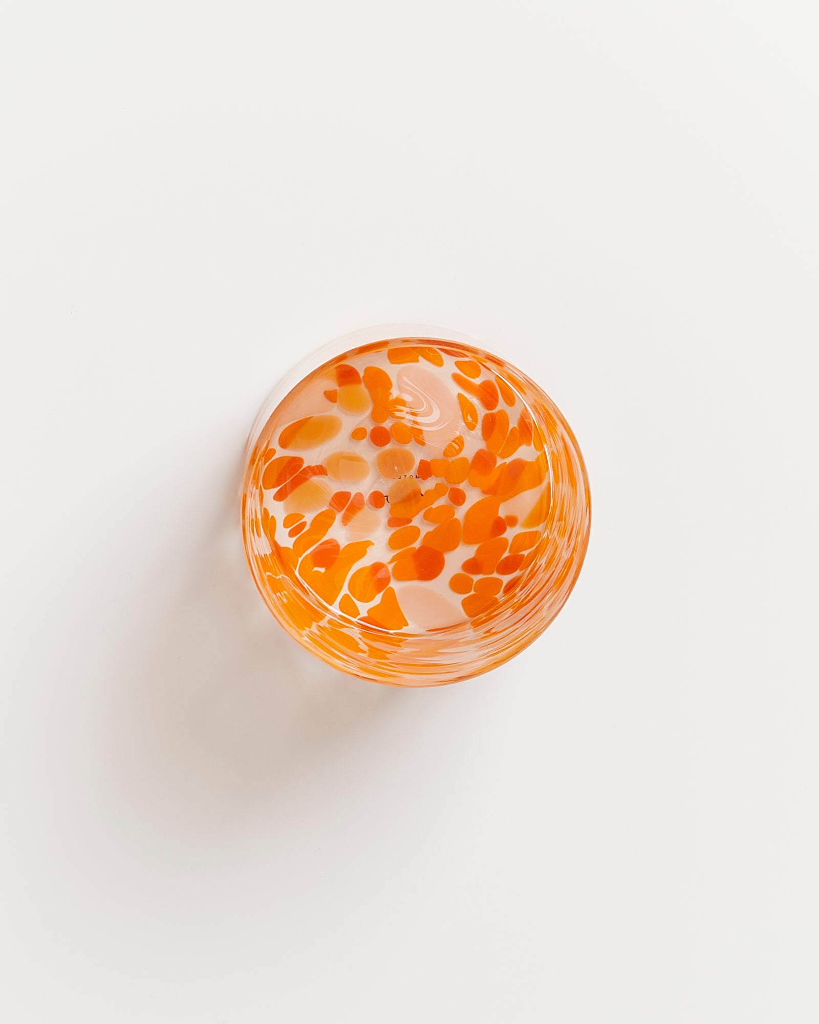 Durchsichtige Glasschale mit orangefarbenen Tupfen auf weißem Hintergrund.