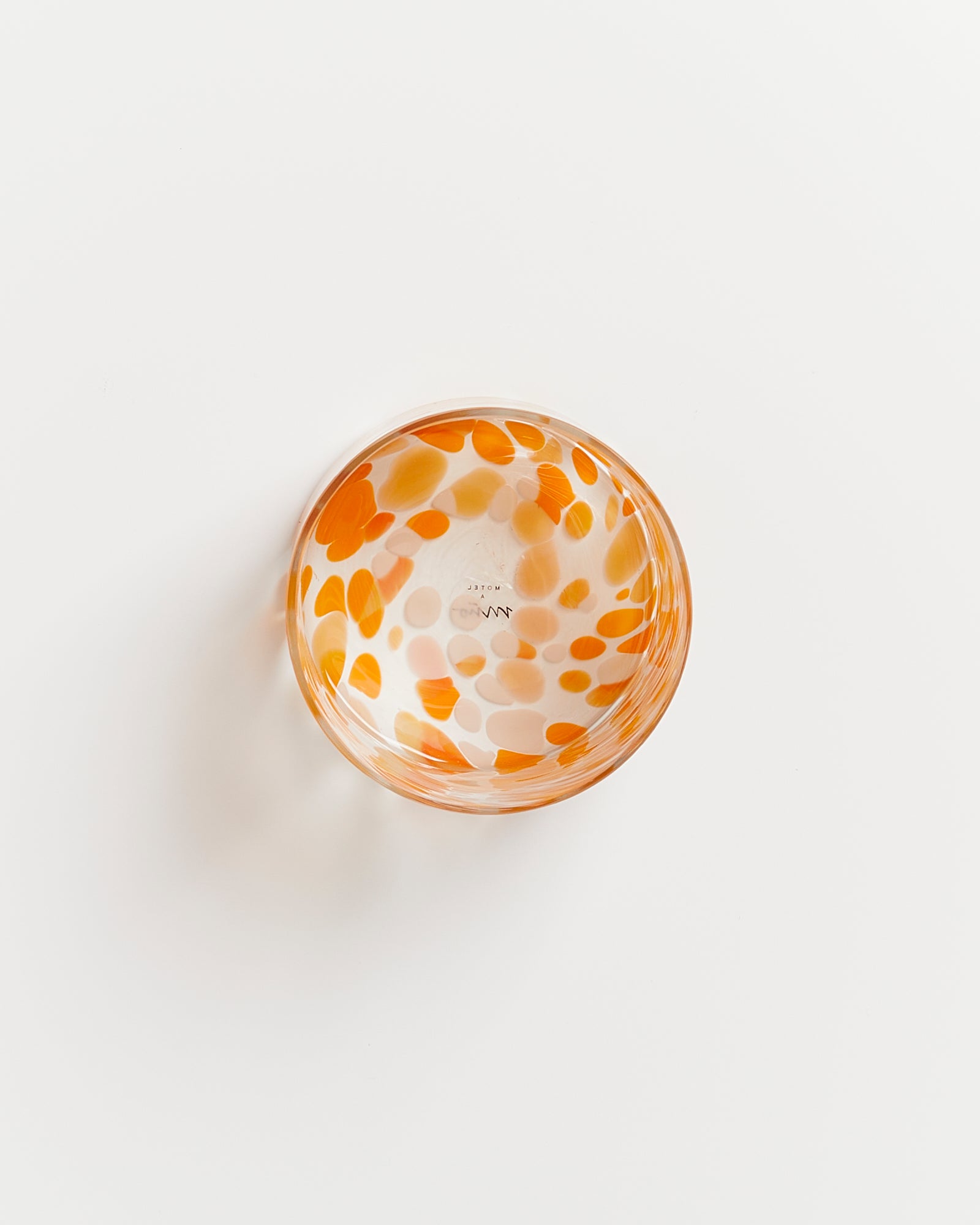Glas mit orangefarbenen Tupfen auf weißem Hintergrund von oben betrachtet.