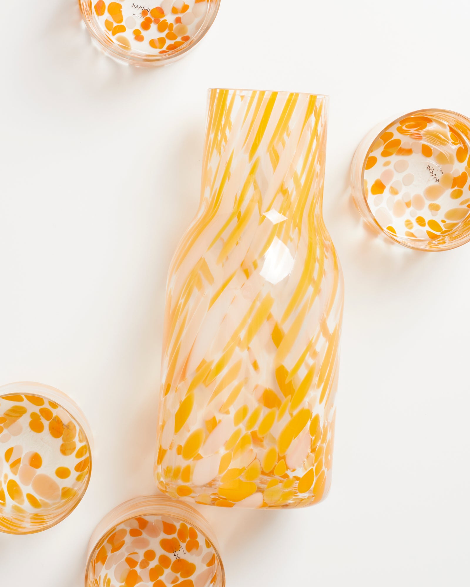 Karaffe und Gläser mit orange-weißem, gepunktetem Muster auf weißem Hintergrund.