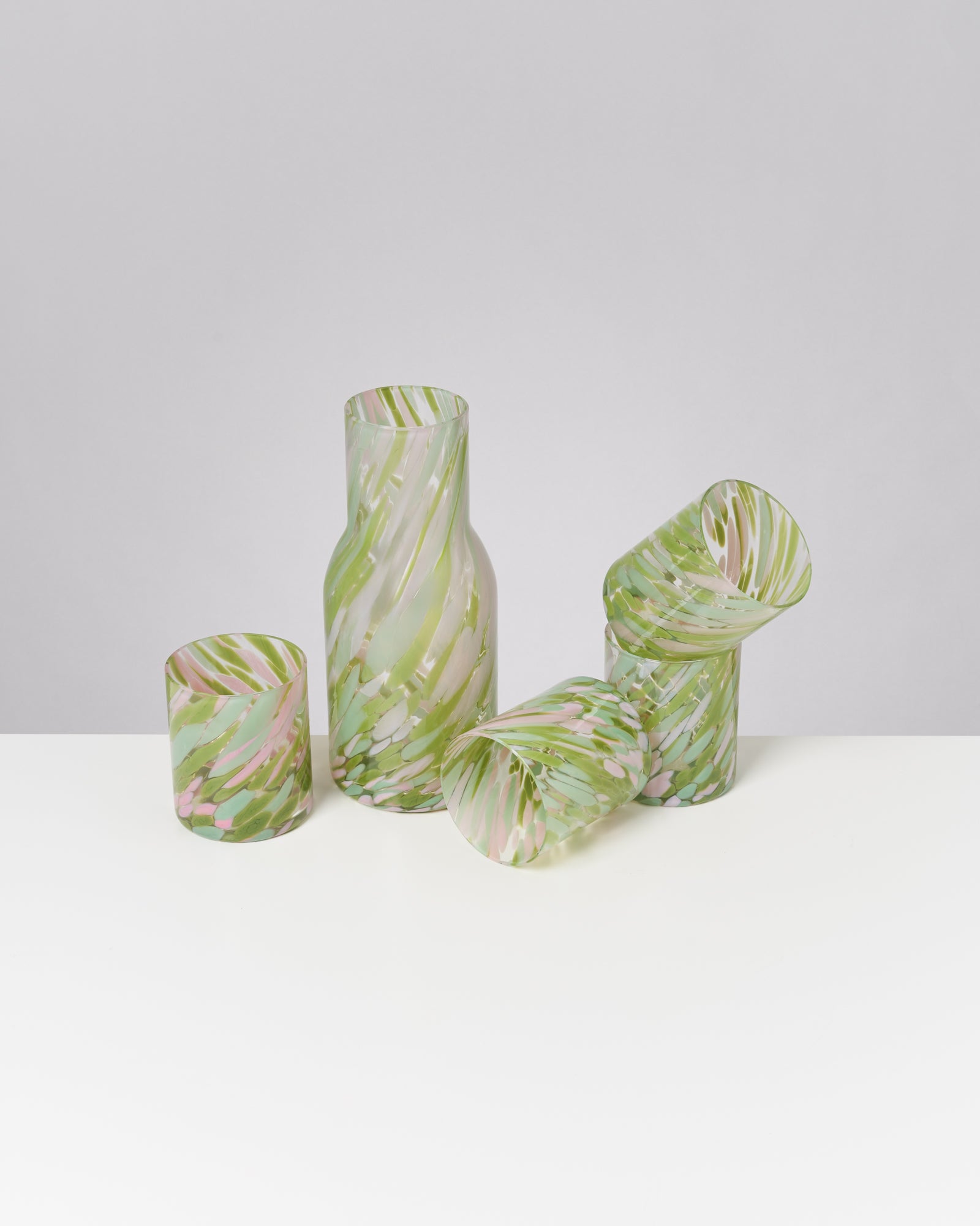 Vier Glasgefäße mit grünen und rosa wirbelnden Mustern auf weißer Oberfläche.