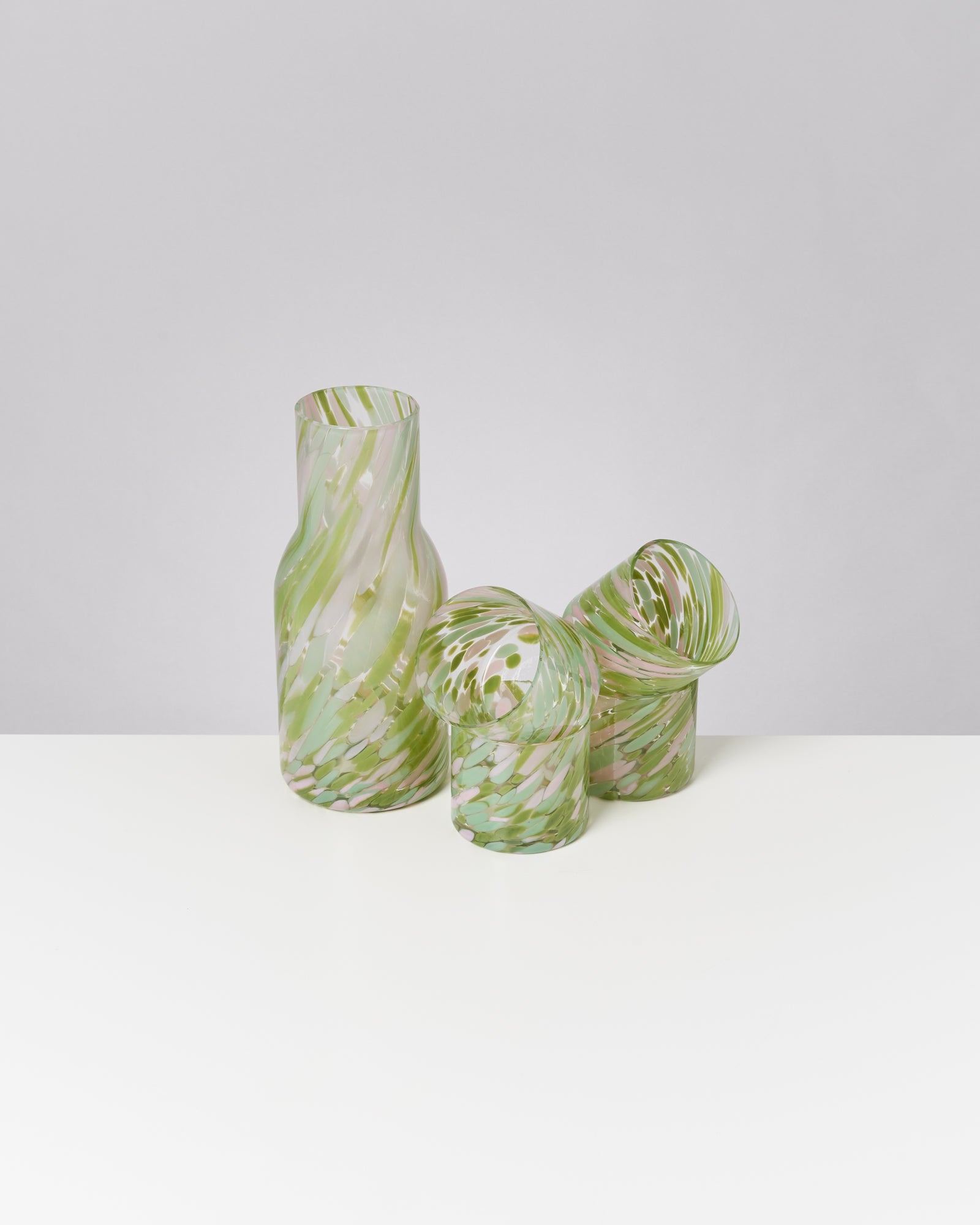 Drei grün gemusterte Glasvasen stehen auf einem weißen Tisch vor grauem Hintergrund.
