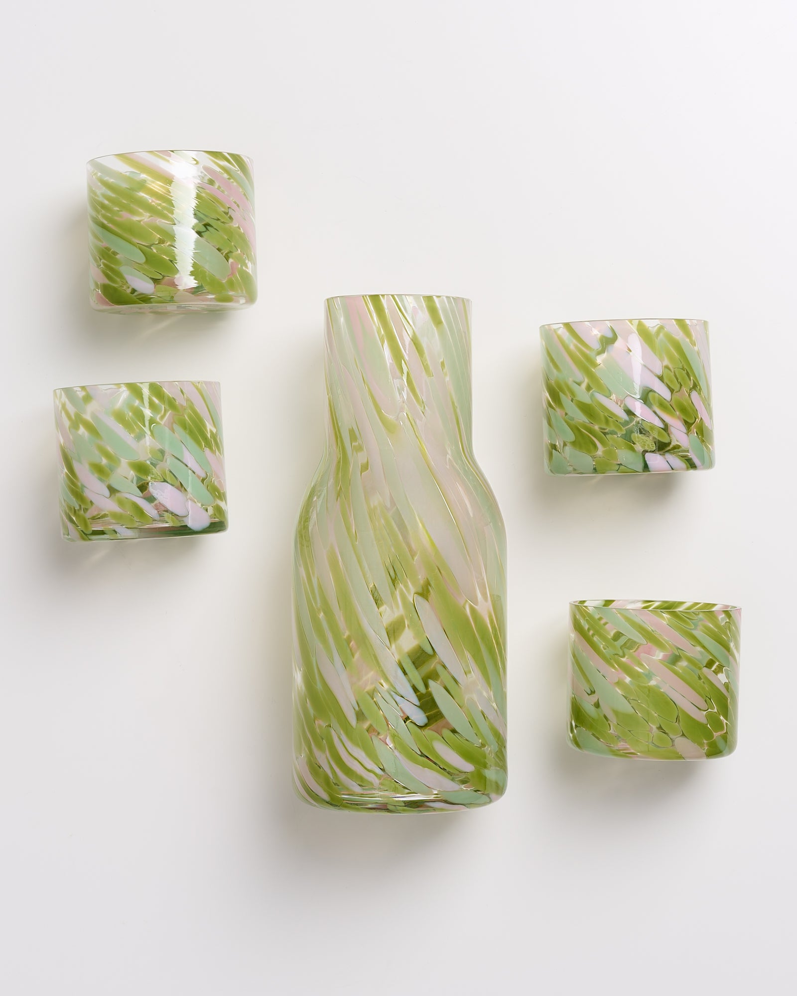 Eine Karaffe und vier Gläser mit grün-rosa marmoriertem Muster auf weißem Hintergrund.
