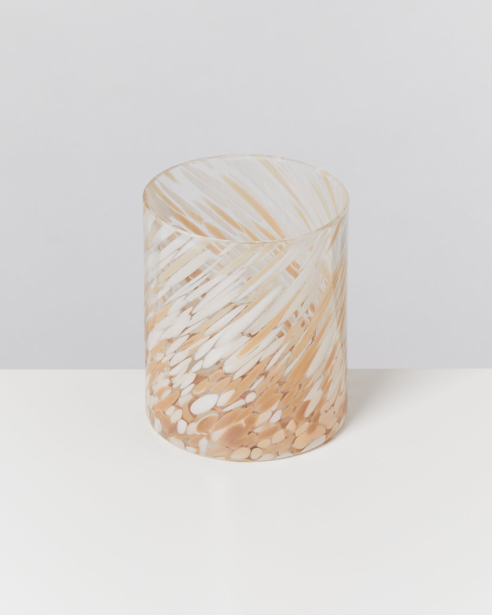 Ein durchsichtiger Kerzenhalter mit beigem und weißem Wirbelmuster steht auf einem weißen Tisch.