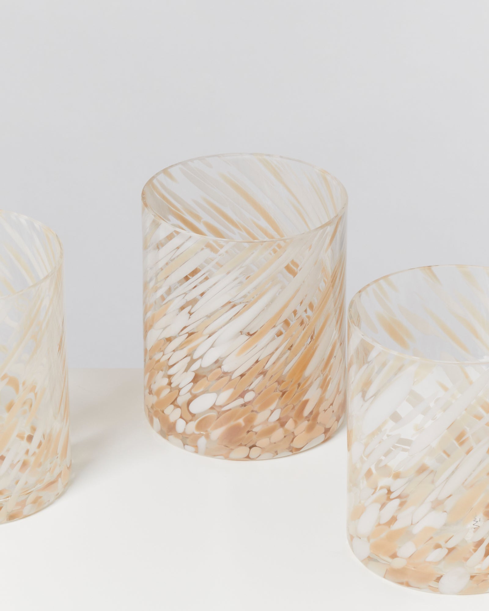 Drei durchsichtige Glasvasen mit weißem und hellbraunem Wirbelmuster vor einem hellen Hintergrund.