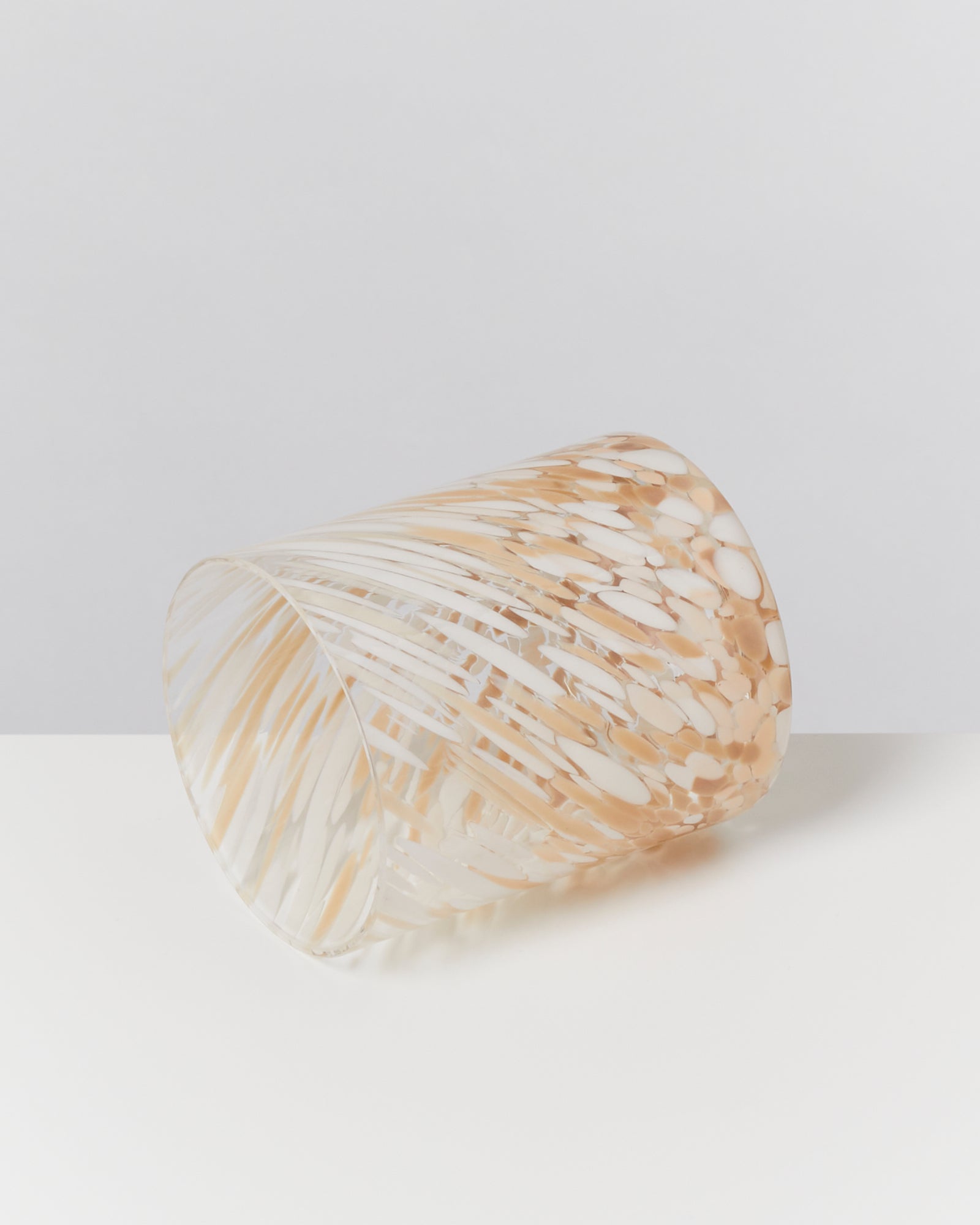 Durchsichtiger Becher mit beigem und weißem Muster liegt schräg auf weißem Untergrund.