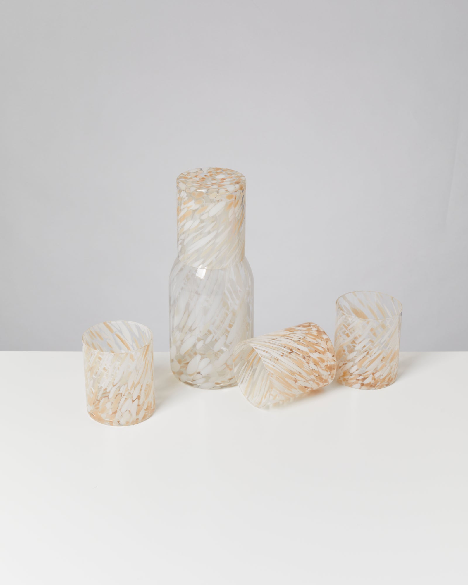 Eine Glasflasche und drei Gläser mit marmoriertem Muster auf einem weißen Tisch.