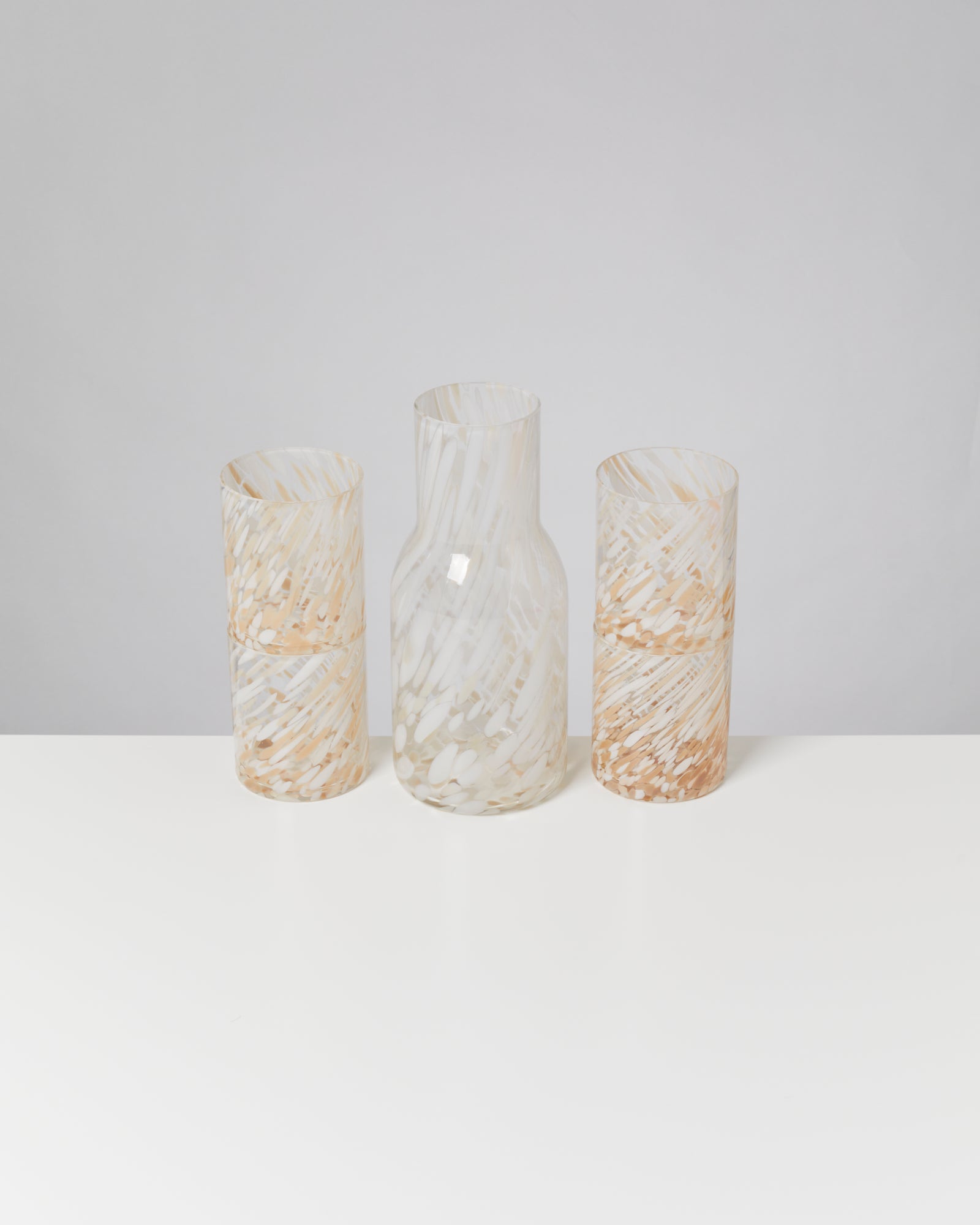Drei Glasbehälter mit marmorierter Textur in Weiß und Beige auf einem weißen Tisch vor neutralem Hintergrund.
