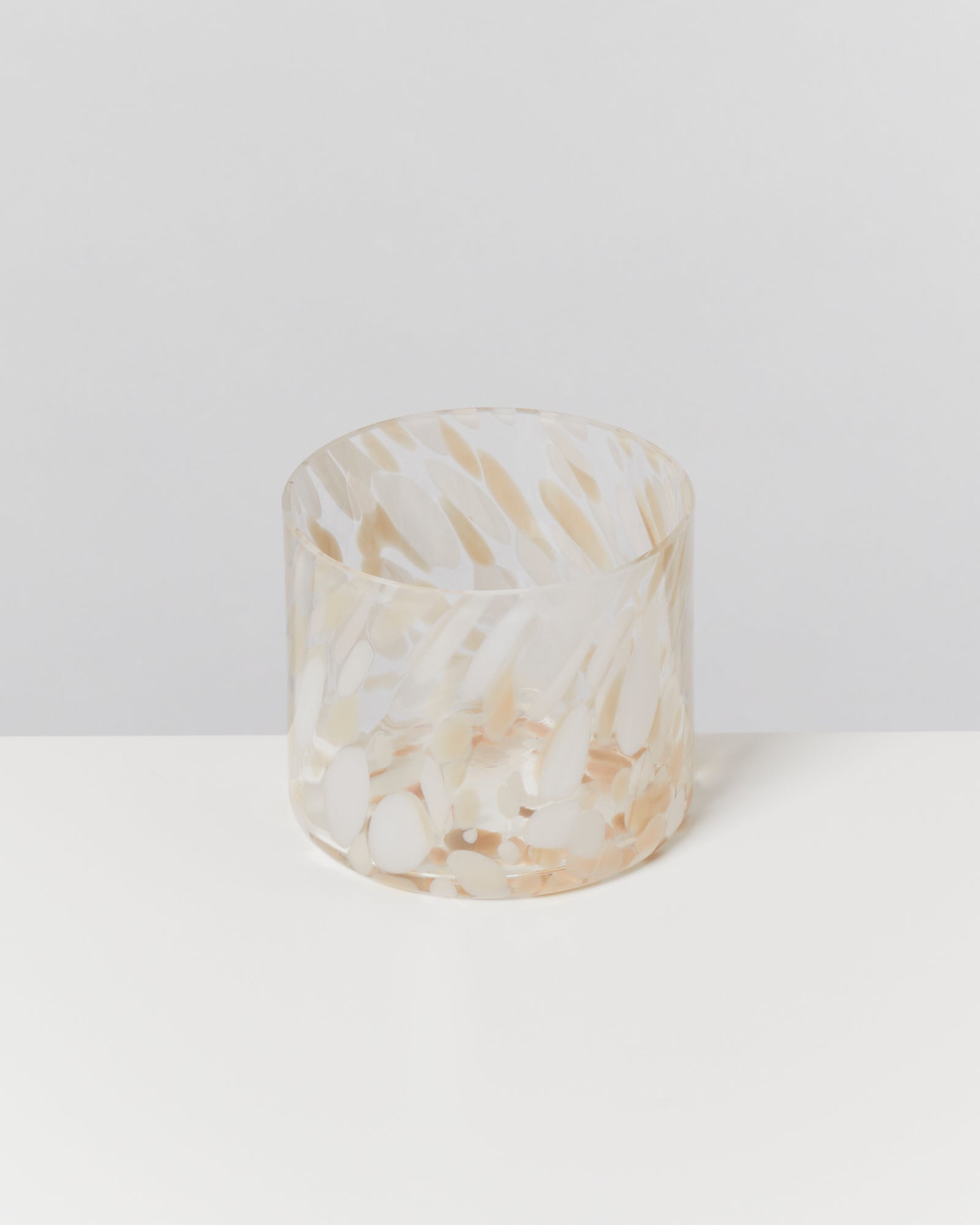 Becher aus getöntem Glas mit marmoriertem Muster auf weißem Hintergrund.