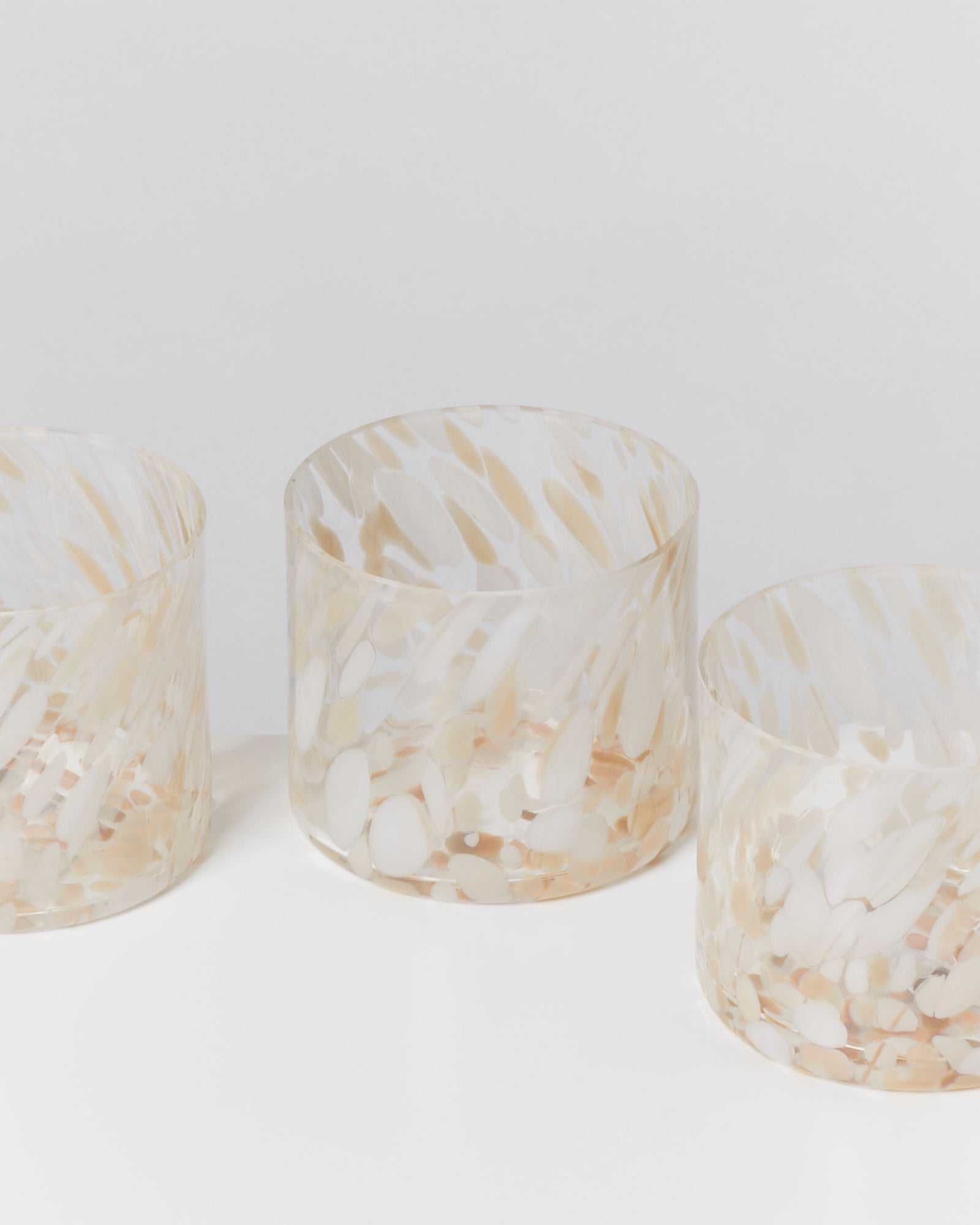 Drei durchsichtige Gläser mit beige und weißen Mustern auf einer weißen Fläche.