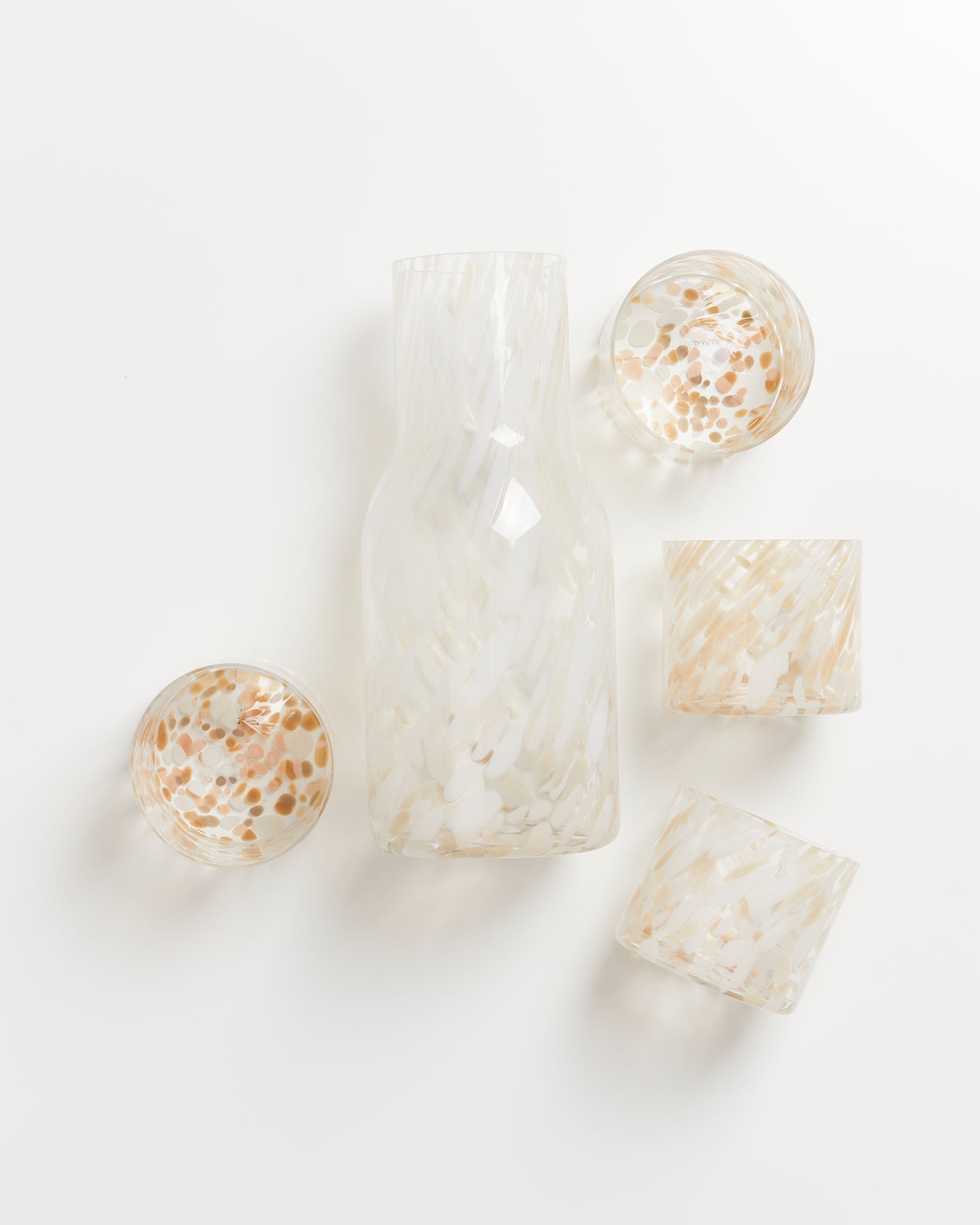 Glasflasche und vier bunte Trinkgläser mit gepunktetem Muster auf weißem Hintergrund.