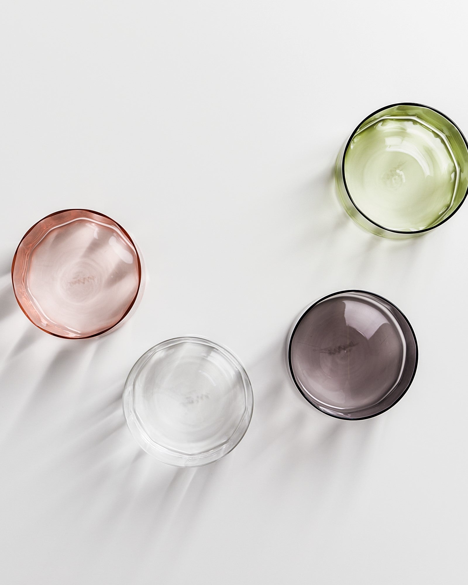 Vier bunte Glasschalen (rosa, grün, klar und dunkelgrau) in diagonaler Anordnung auf weißem Hintergrund.