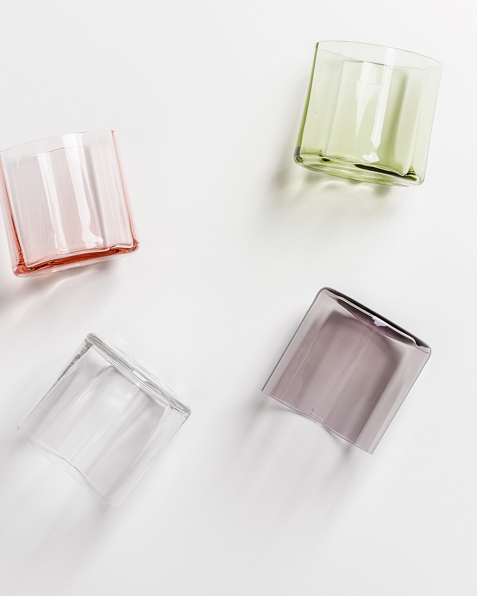 Vier bunte, quadratische Gläser liegen auf einer weißen Oberfläche.